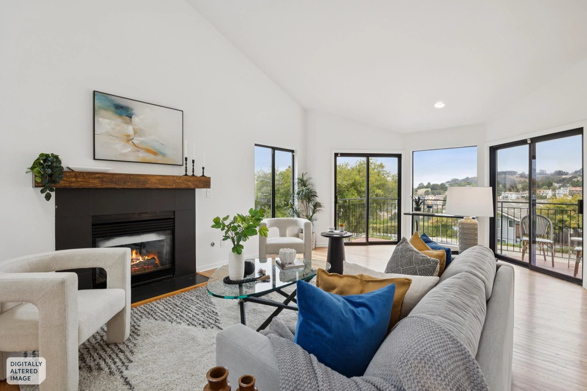 Living room with white walls, a fireplace with a wooden mantel and black surround, large windows with black frames, beige and blue cushions on a white sofa, a cream armchair, a glass coffee table with decorative items, a patterned rug, and garden views outside.