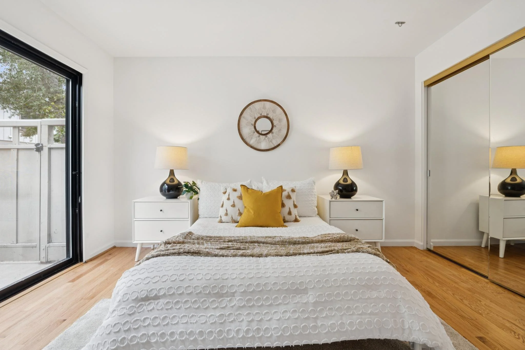 Bedroom with white walls, a bed with white and yellow pillows, two nightstands with lamps, and a large mirror closet doors.