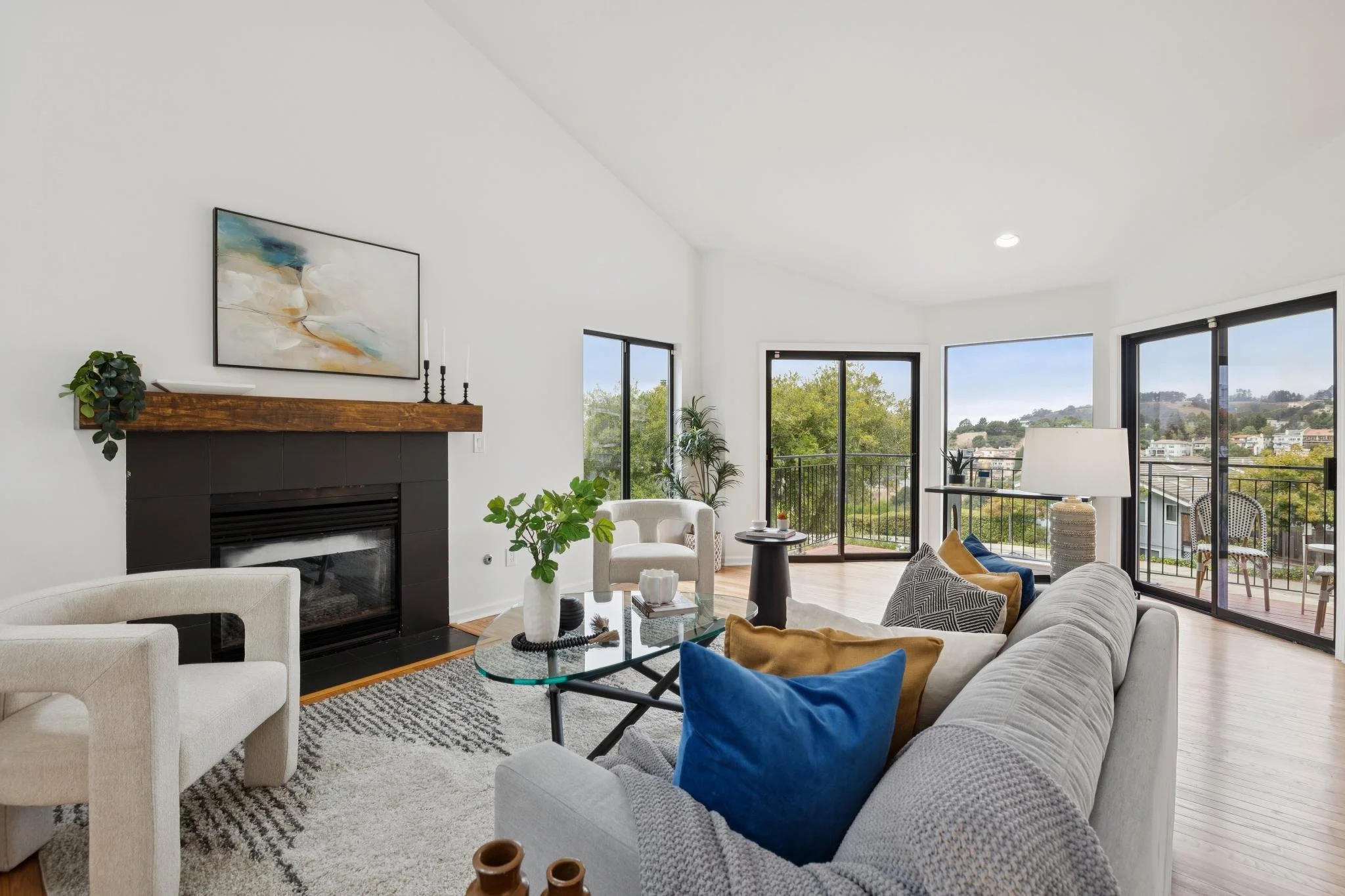 Modern living room with white walls, large windows, beige and blue furniture, fireplace, and indoor plants.