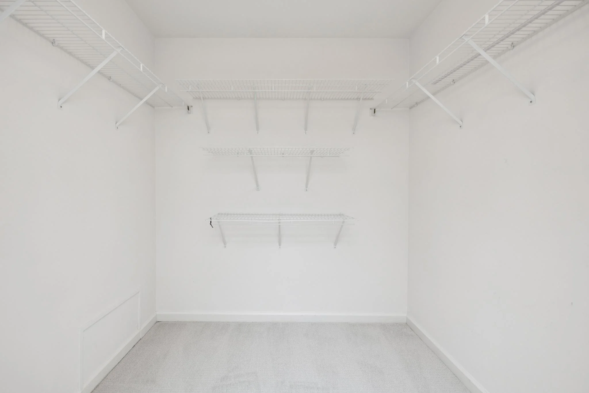 Empty walk-in closet with white wire shelves on all three walls and a gray carpeted floor.