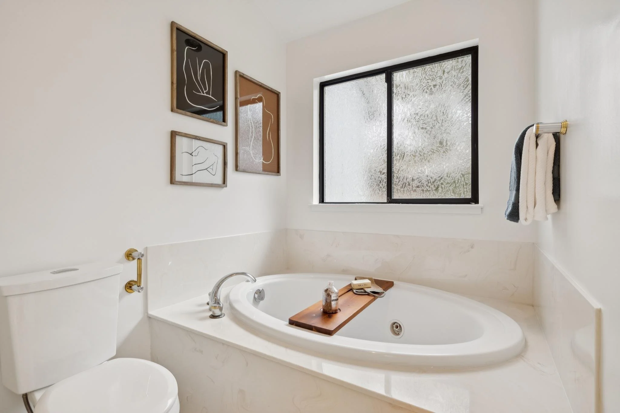 Bathroom with a white bathtub, a toilet, artwork on the wall, and a window with frosted glass.