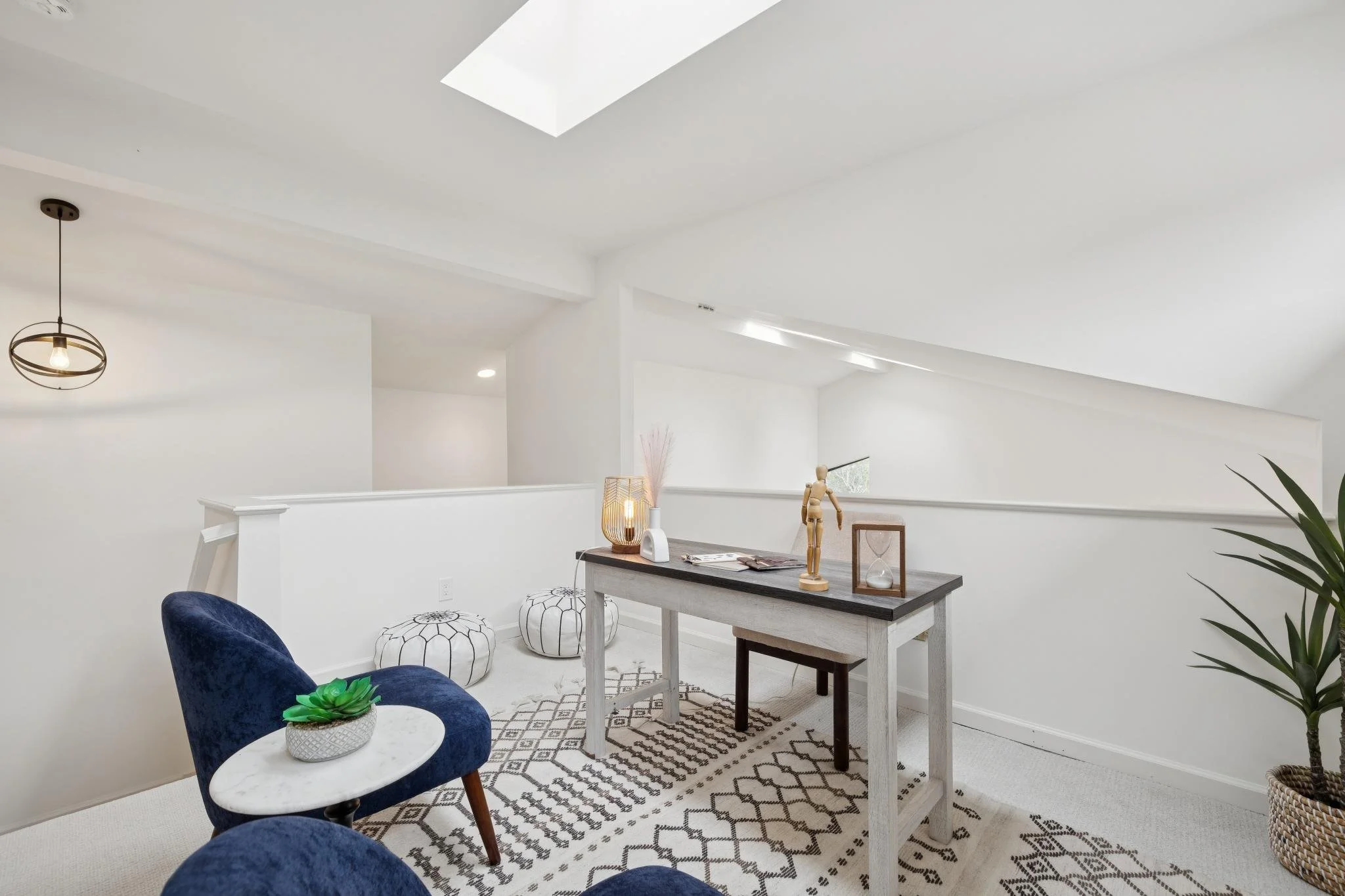 Modern dining room with white walls, skylight, round pendant light, wooden table with decorative items, navy blue velvet chairs, patterned rug, and green plant.