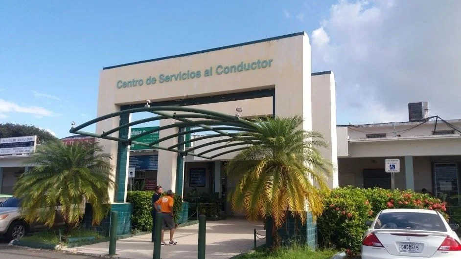 Building with Spanish sign 'Centro de Servicios al Conductor' and a parking lot with cars and palm trees in front.
