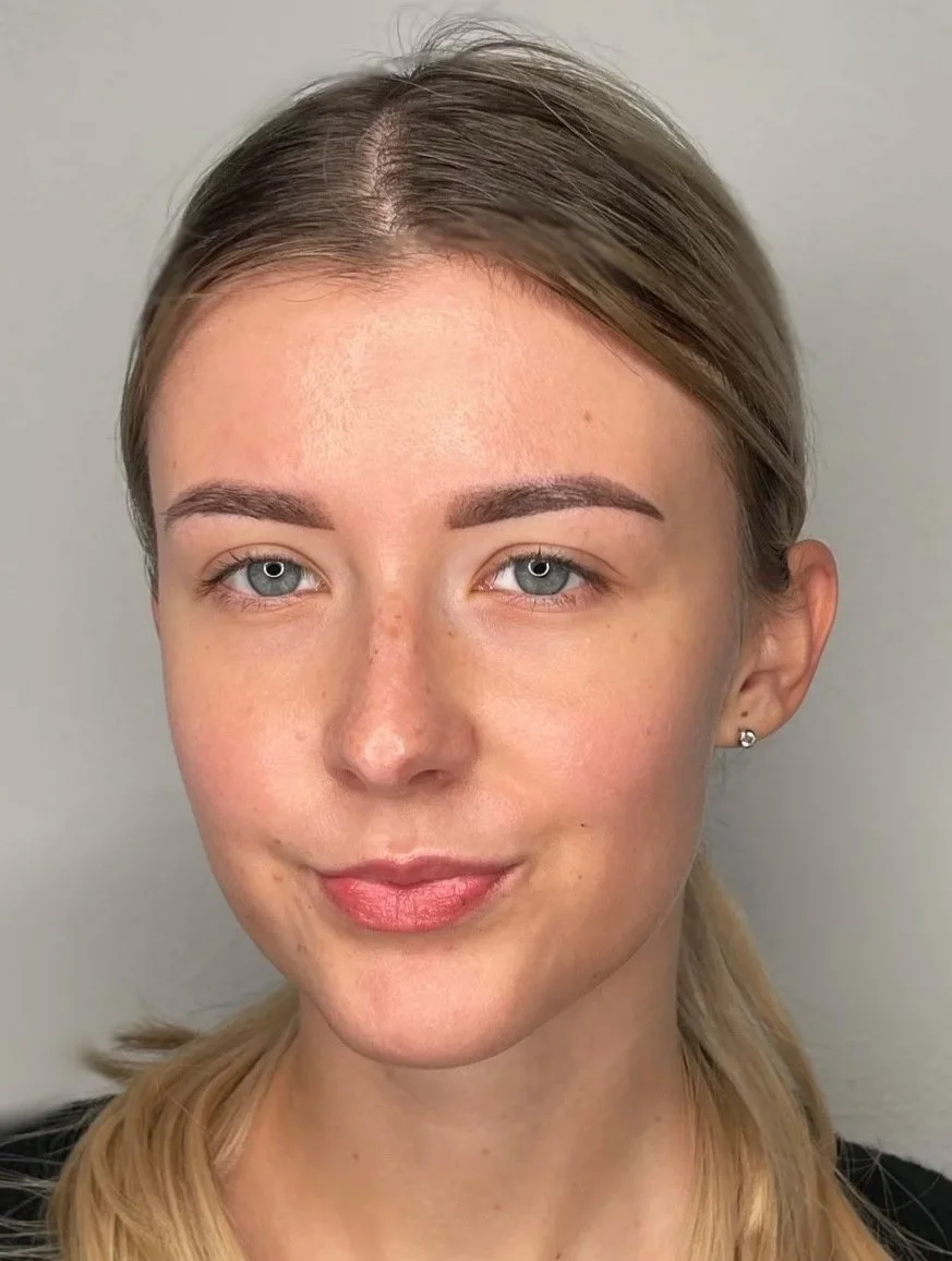 Nahaufnahme eines lächelnden jungen Mädchens mit blonden Haaren, blauen Augen und kleinen Ohrringen vor einem neutralen Hintergrund.