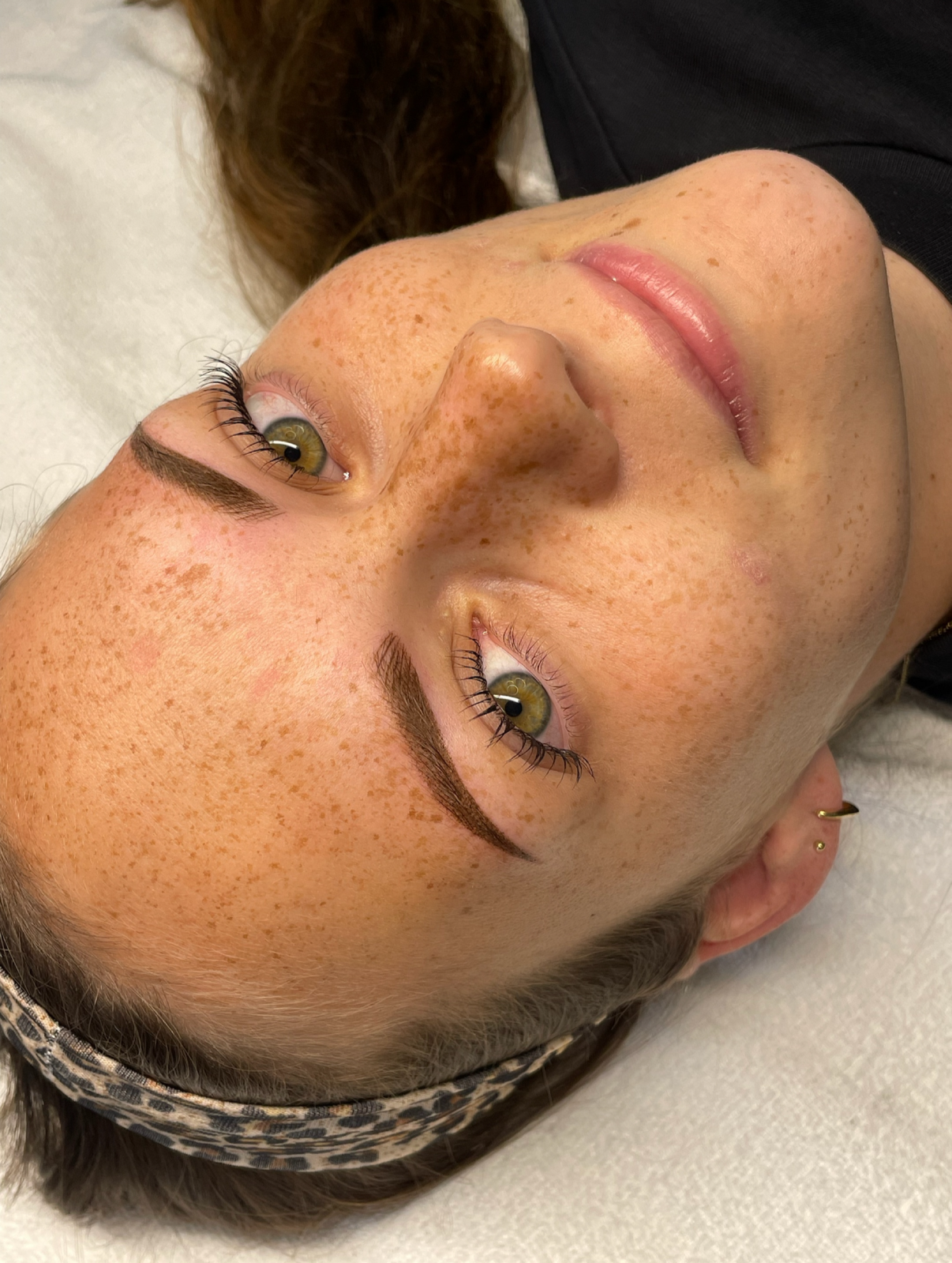 Nahaufnahme eines Frauengesichts mit Sommersprosse, grün-gelben Augen und braunen Haaren mit Haarreif.