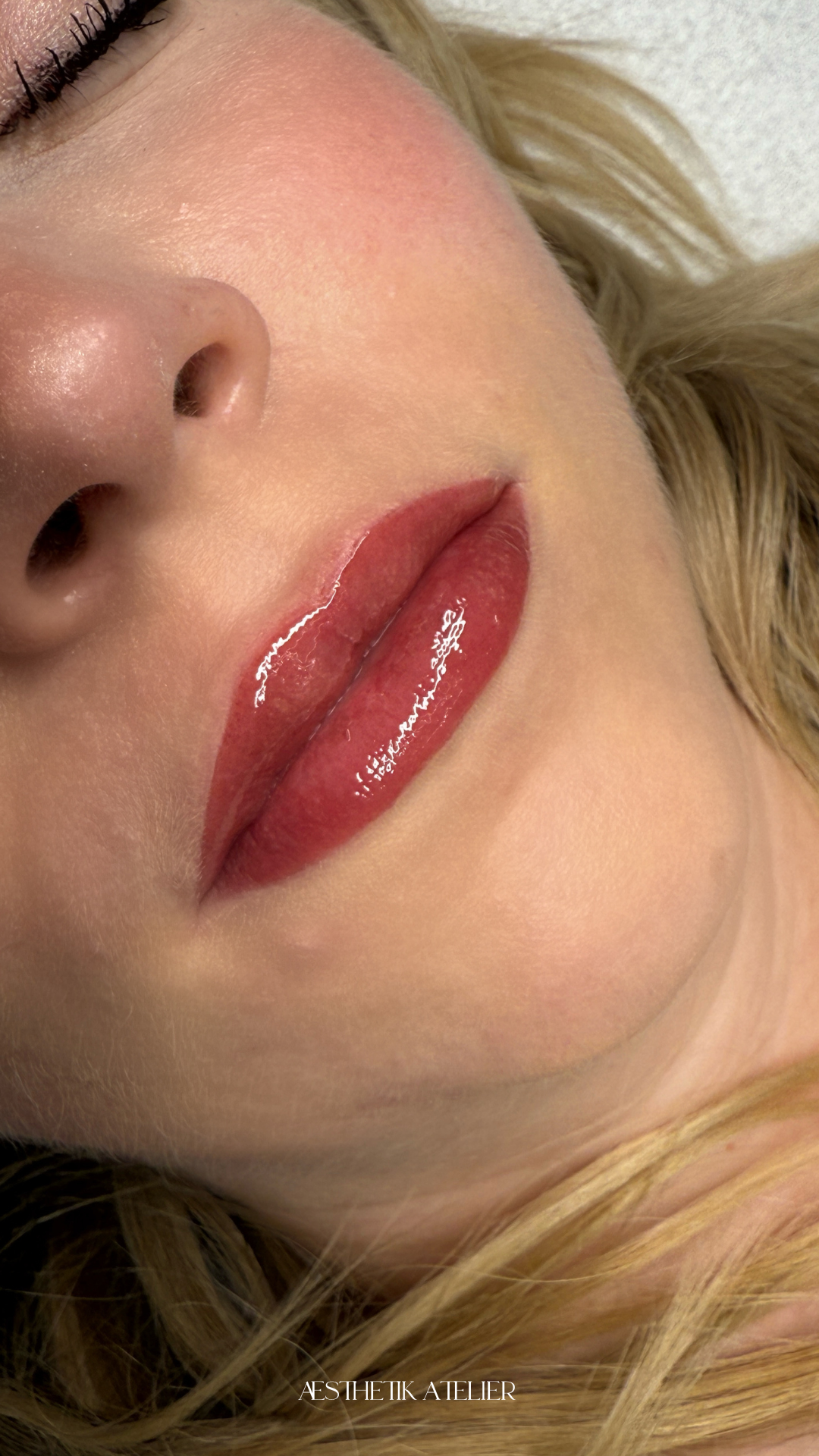 Nahaufnahme eines Gesichts mit betonten roten Lippen und natürlicher Haut, teilweise sichtbar eine Nase und blonde Haare.