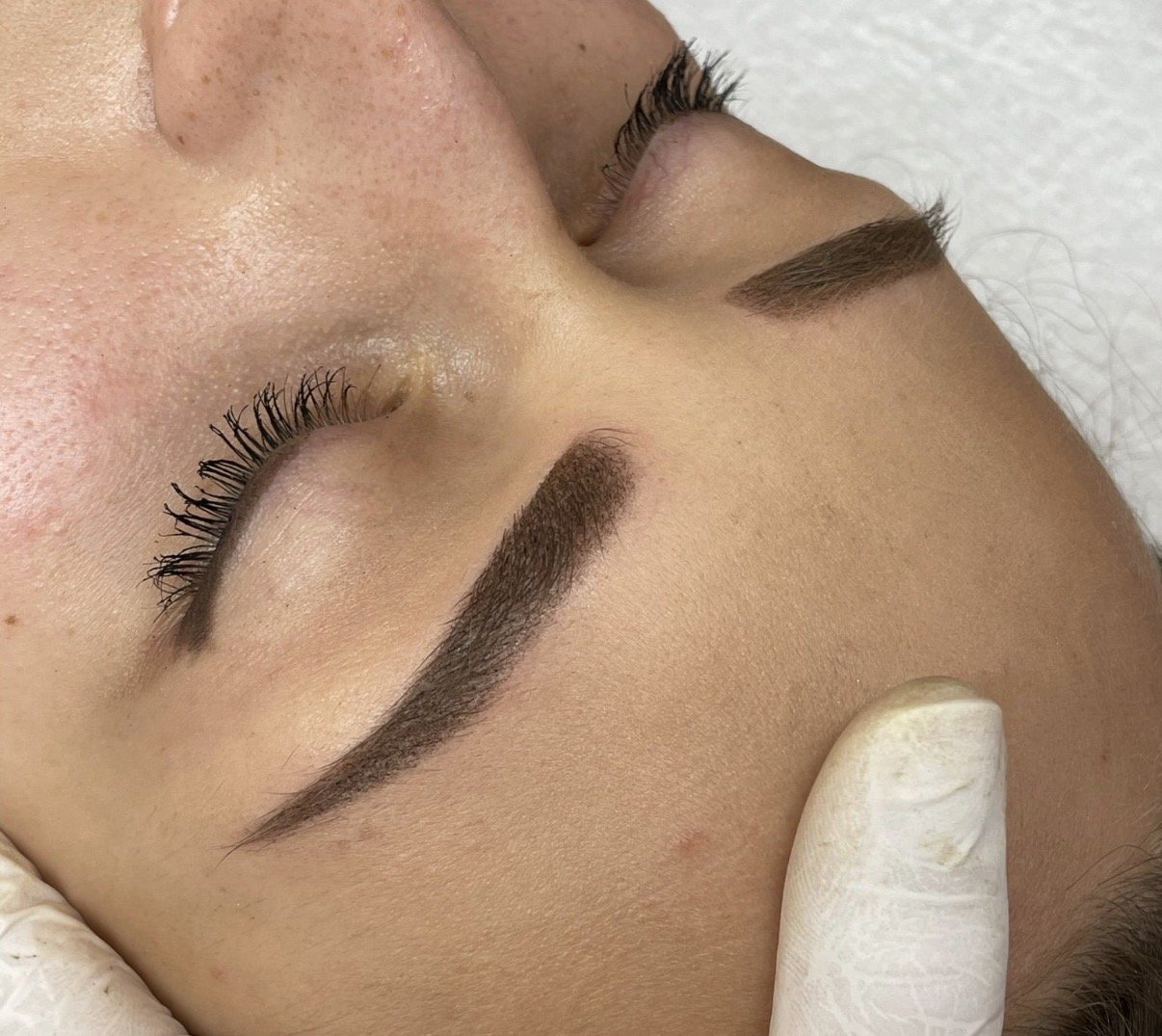 Nahaufnahme von einem Gesicht, auf dem im Bereich der Augenbrauen und Wimpern eine kosmetische Behandlung durchgeführt wird.