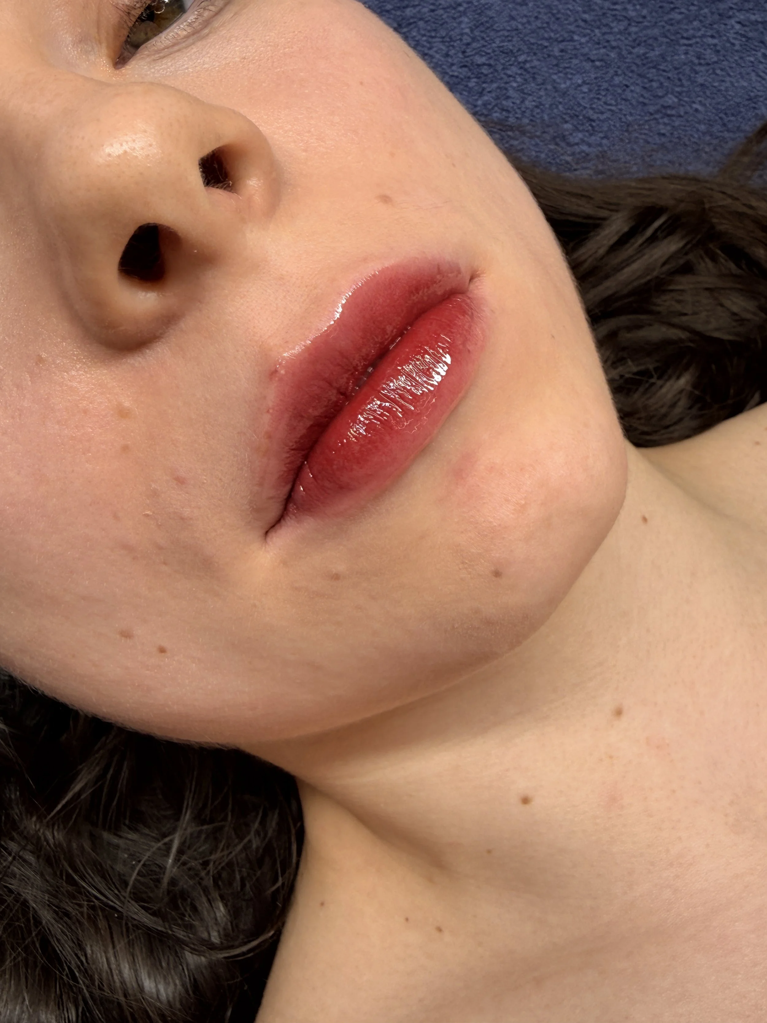Nahaufnahme eines Gesichts mit Blick auf Lippen, Nase und Teil des Auges, geschminkte Lippen, dunkle Haare, Haut mit kleinen Muttermalen.