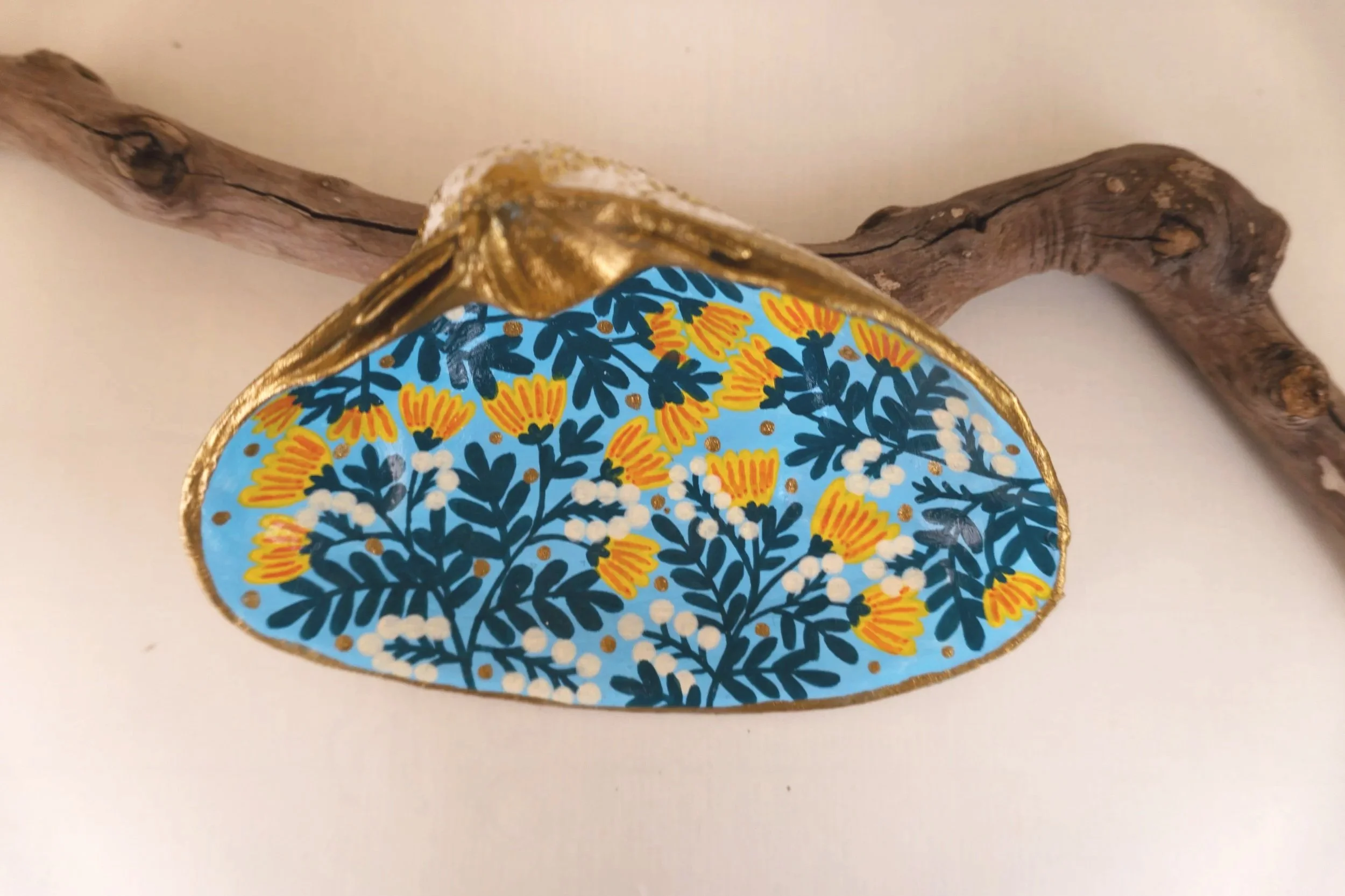 Decorative plate with blue background and orange, yellow, and white floral pattern, placed on a branch against a plain background.