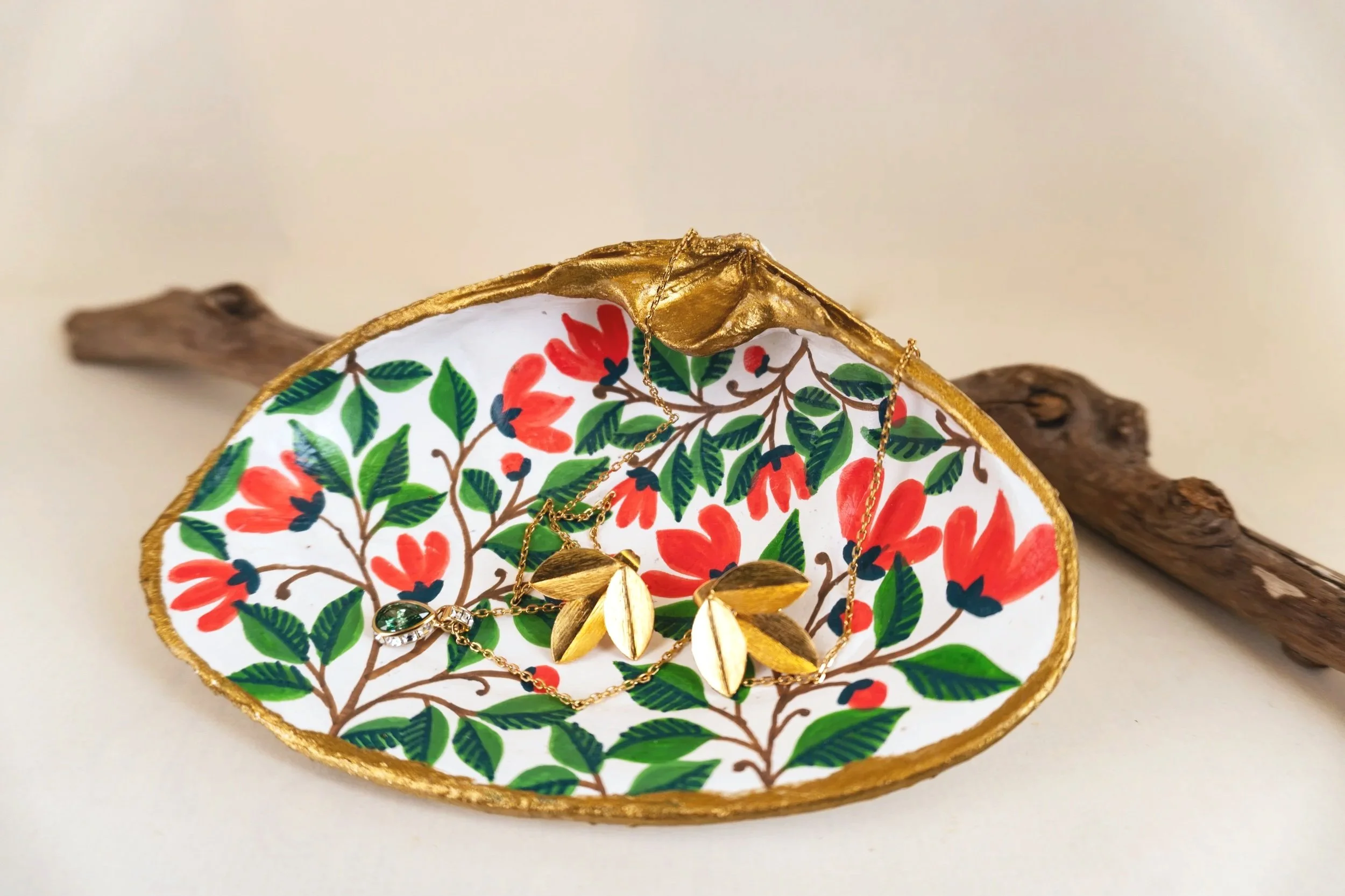 Decorative jewelry display with gold and green necklace on a floral patterned surface, next to a piece of driftwood on a plain background.