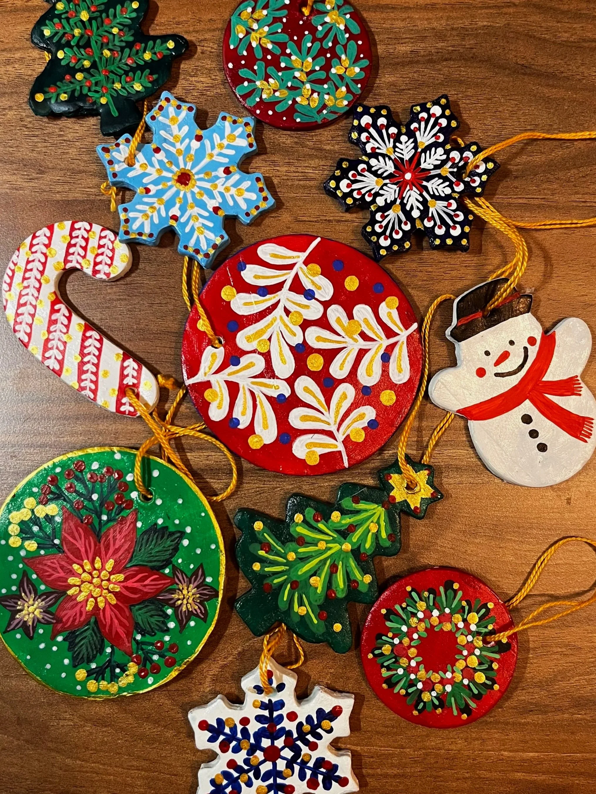 Colorful Christmas ornaments on a wooden surface, featuring various festive designs such as snowflakes, holly, Christmas trees, and a snowman.