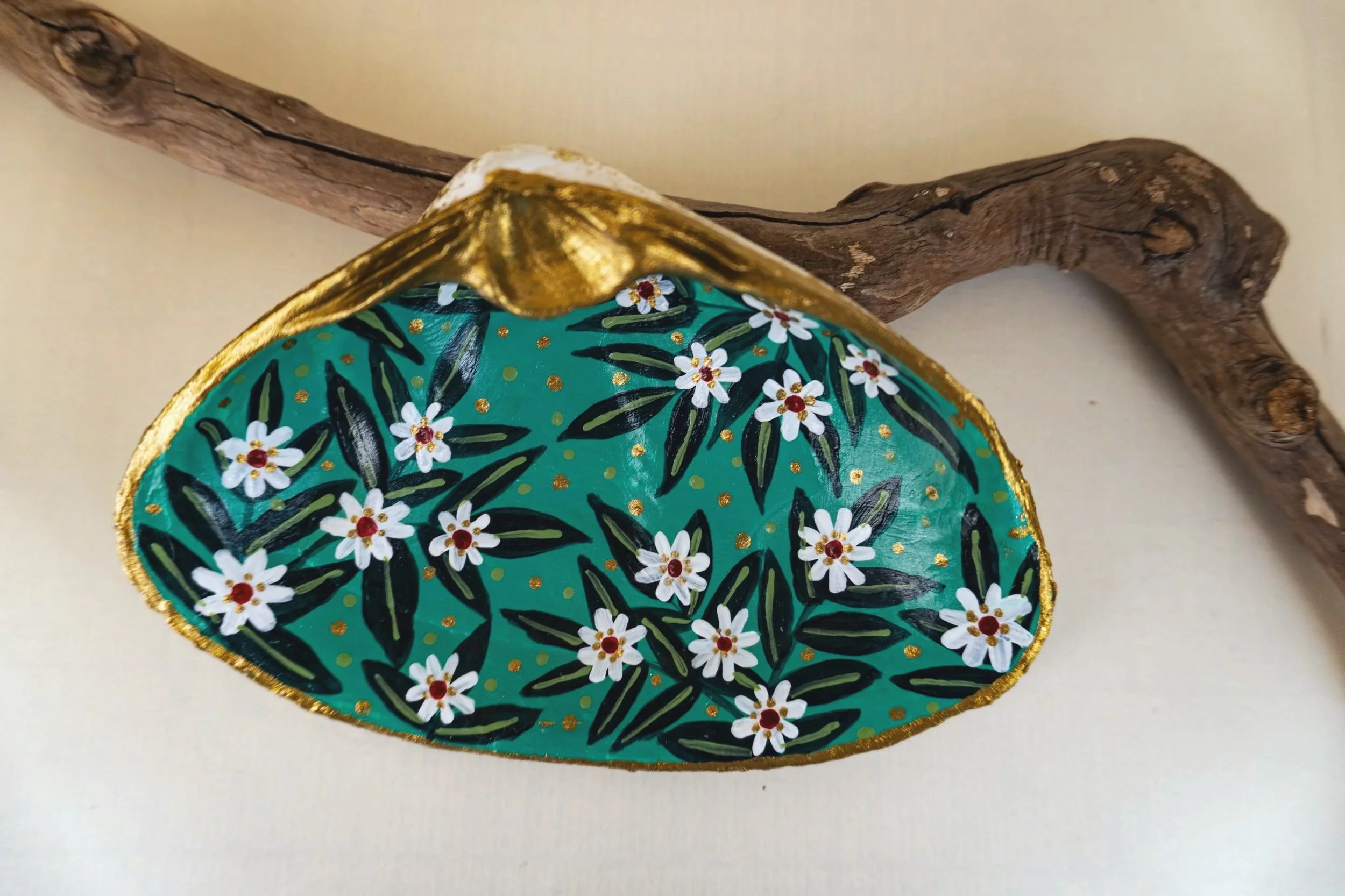 Decorative oval-shaped object with a floral pattern, gold trim, and a golden edge resting on a twisted piece of wood.