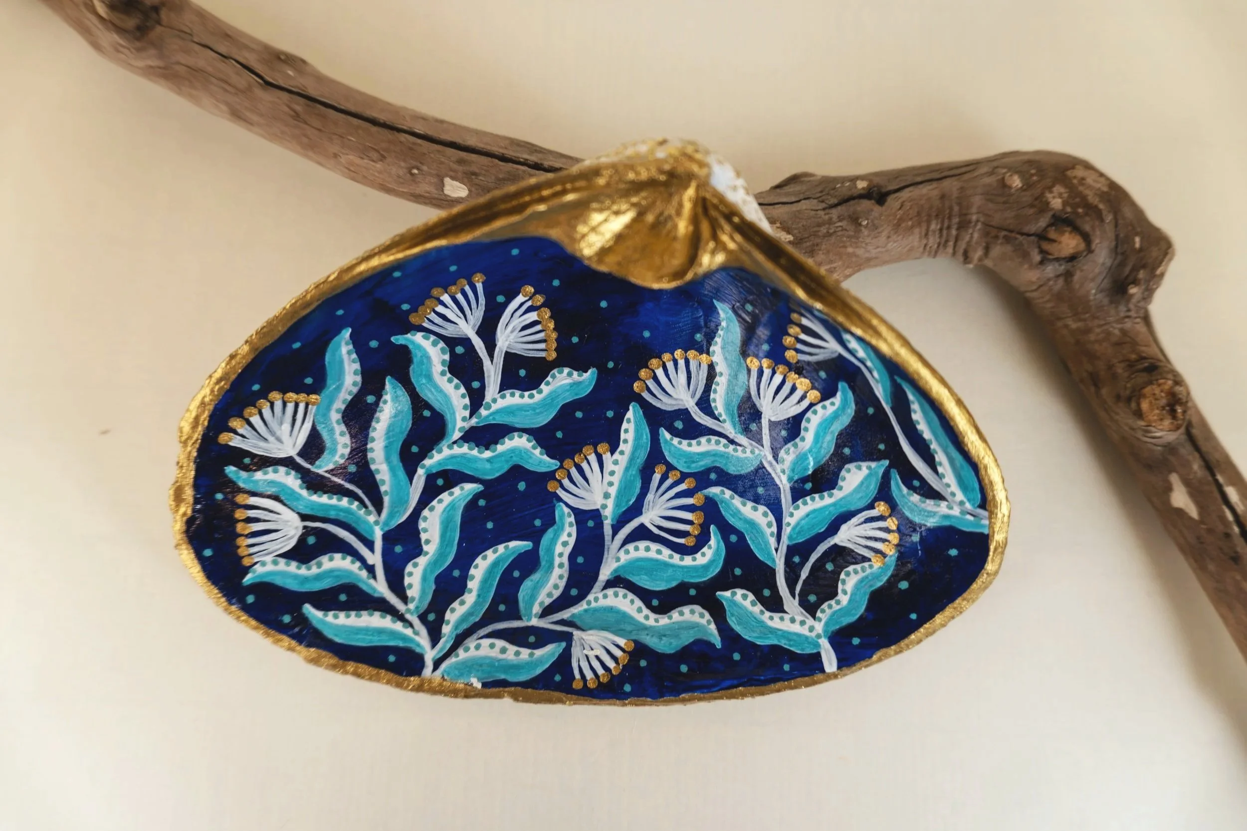 Decorative wooden piece with a painted floral pattern in blue, white, and gold, mounted on a twisted tree branch.
