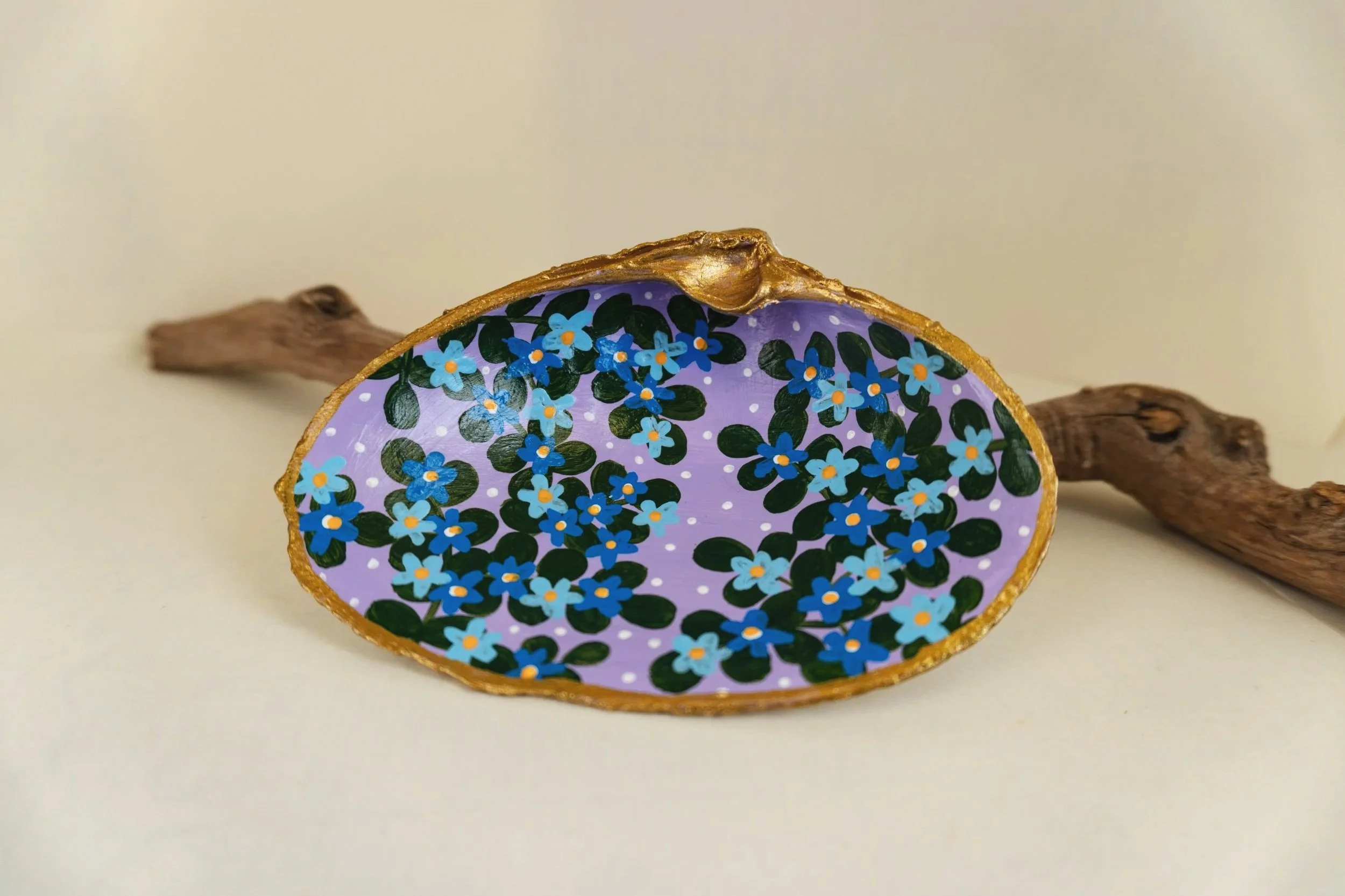 A cross-section of a decorated tree branch with floral artwork on the interior surface, showing blue flowers and green leaves; the branch has a natural, rough bark exterior.