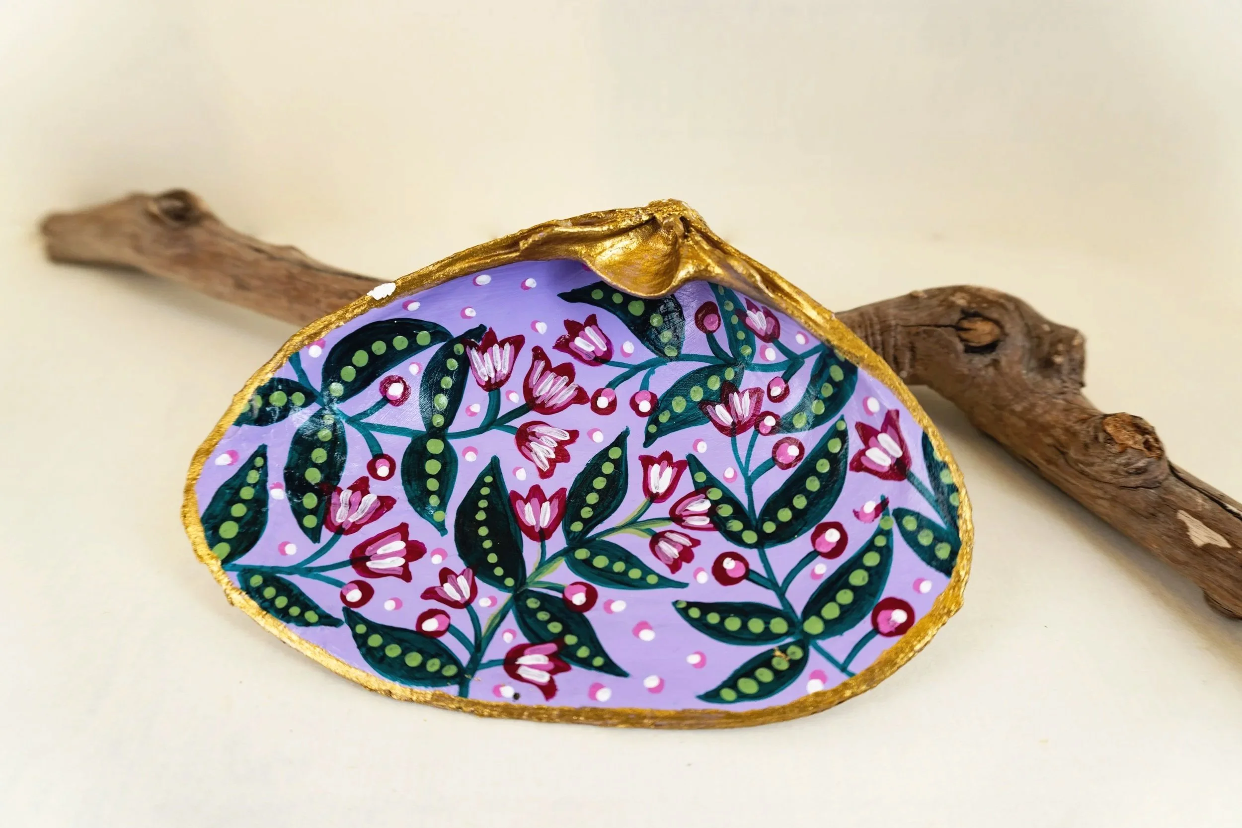 Colorful decorative object with intricate floral patterns, edged with gold, with two pieces of driftwood or natural wood placed beside it on a light background.