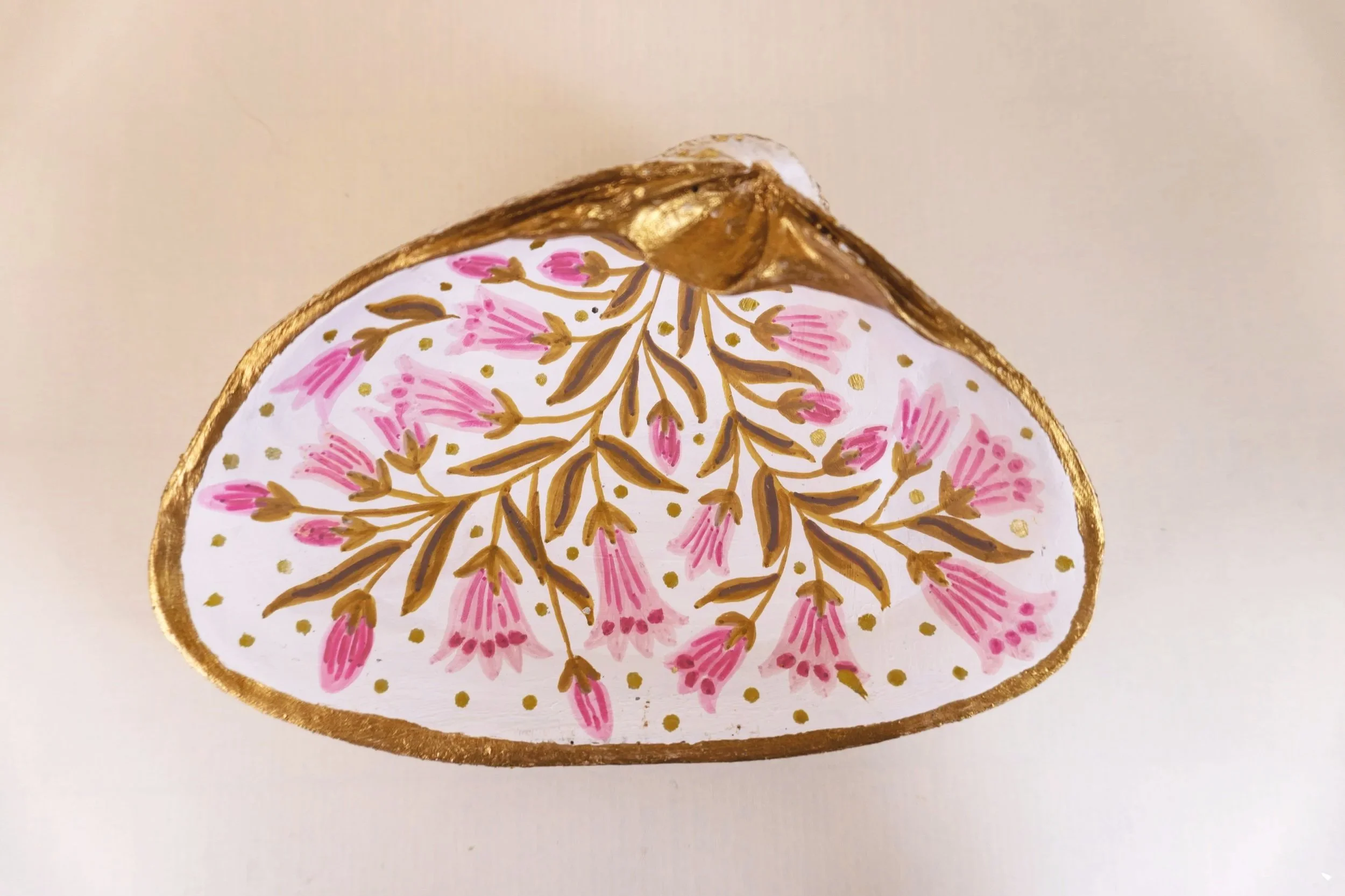 Decorative ornament with a white background, gold outline, pink floral pattern, and intricate gold and brown leaf design in the center.