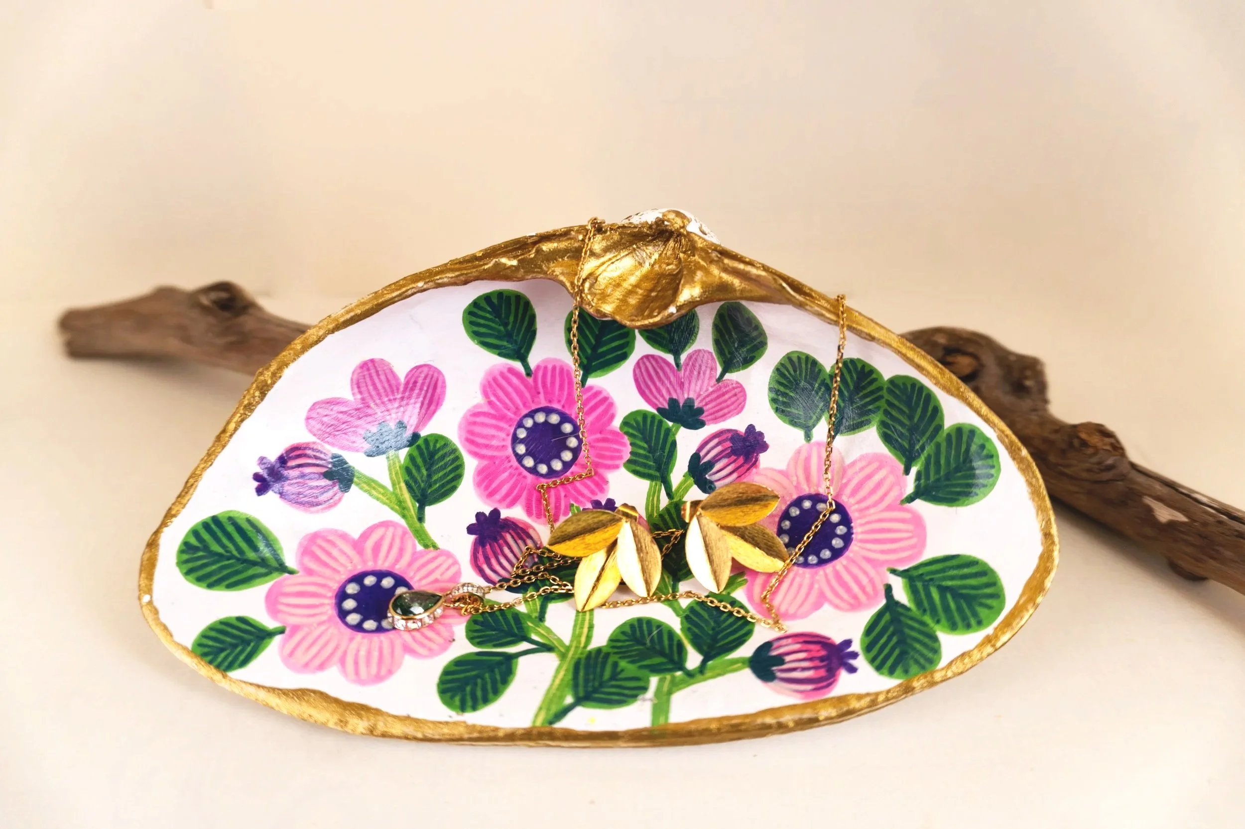 Decorative jewelry tray with floral pattern, holding gold and chain necklaces, set on a wooden branch.