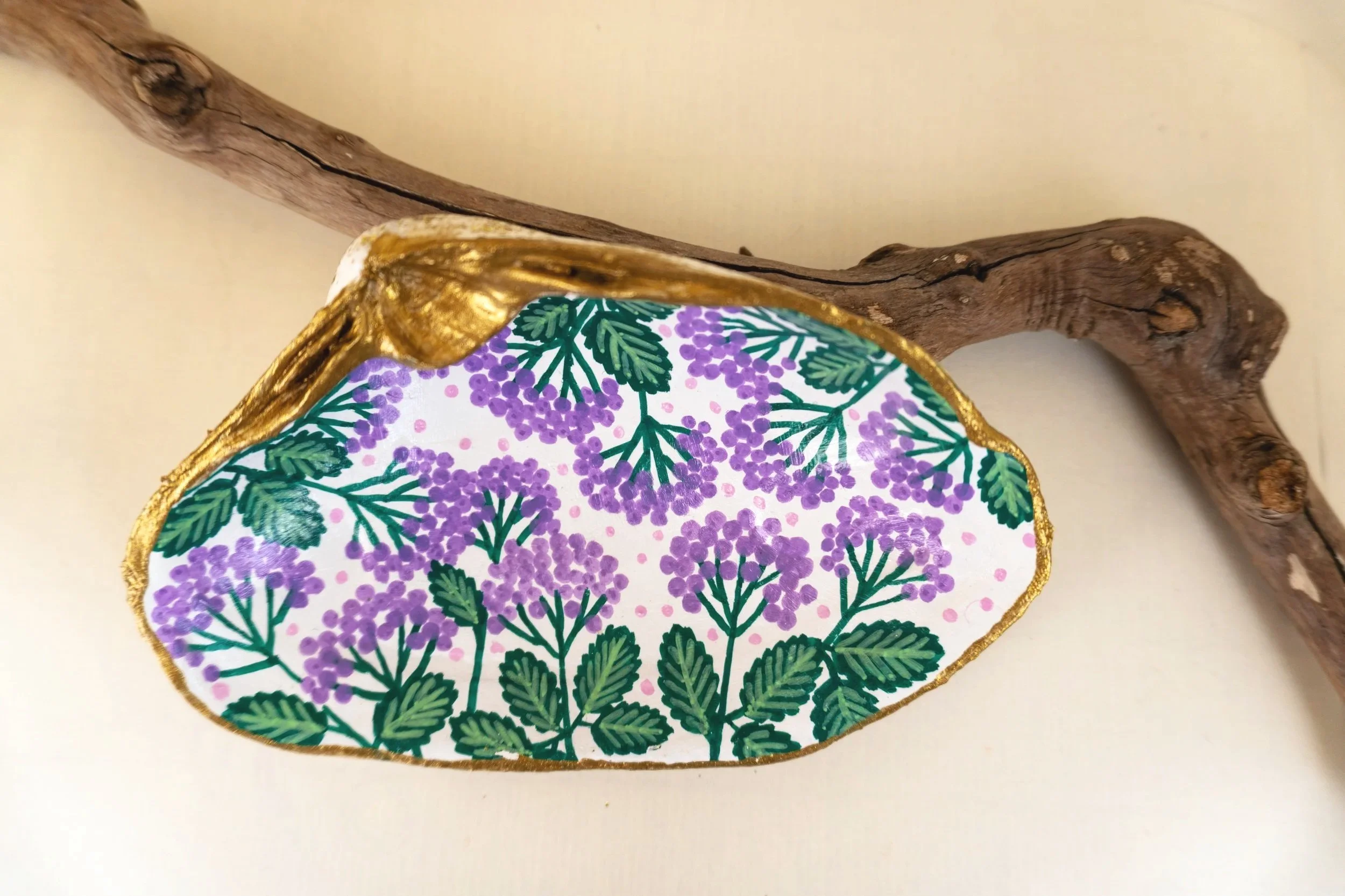 Decorative plate featuring purple berries and green leaves, edged with a gold rim, resting against a piece of curved, textured wood.