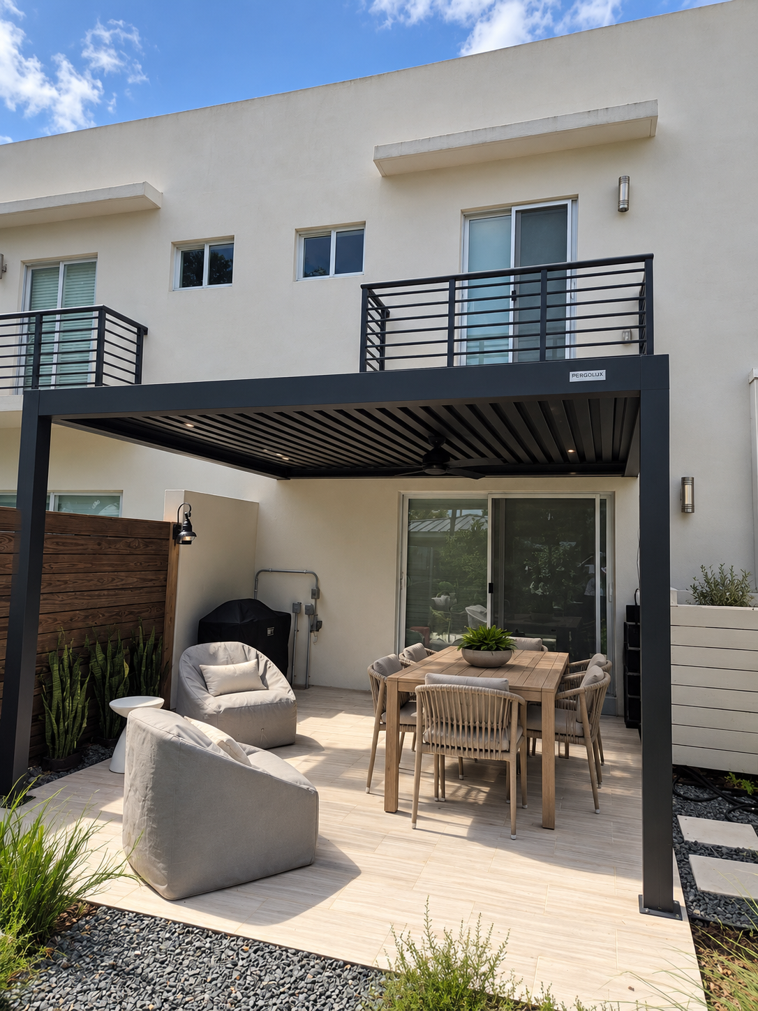 Outdoor patio with dining table, chairs, and lounge seating beneath a modern black pergola, adjacent to a white residential building with small balconies, sliding glass door, and potted plants.