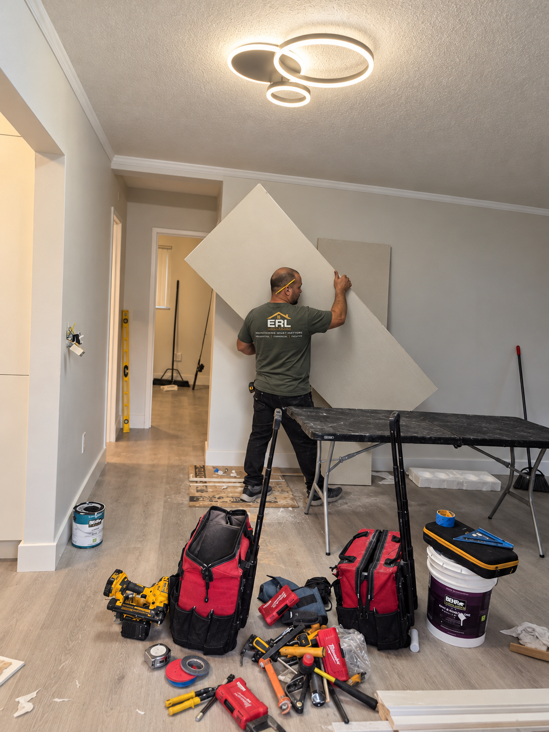 A man installing or repairing drywall in a living room space with tools and equipment on the floor.