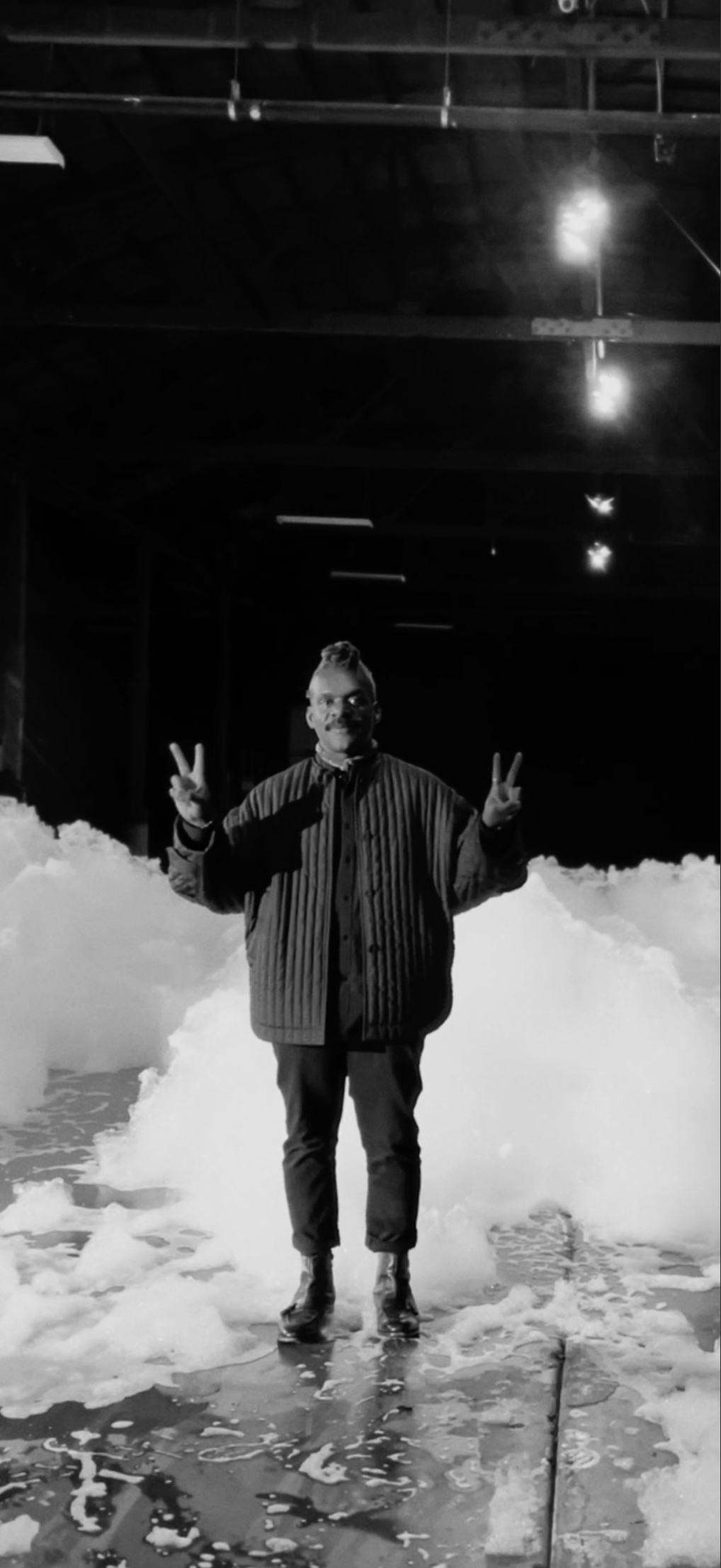 Sean standing on in a warehouse filled with foam, posing with peace signs in both hands.