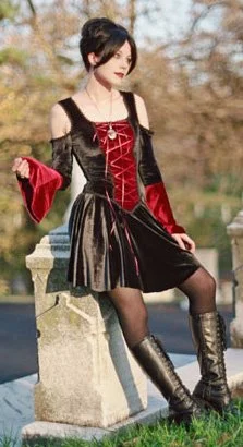 Woman in black and red Gothic-style dress sitting by a stone railing outdoors during autumn.