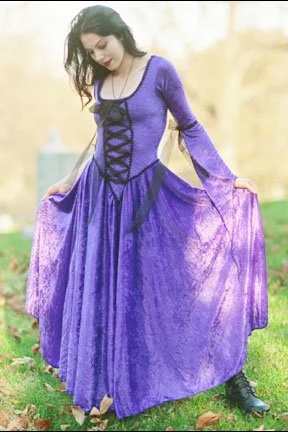 A woman in a purple medieval-style dress outdoors, holding the sides of her gown.