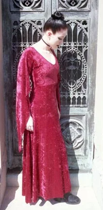 A woman in a long, pink velvet dress with a high bun hairstyle standing in front of a decorative metal gate.