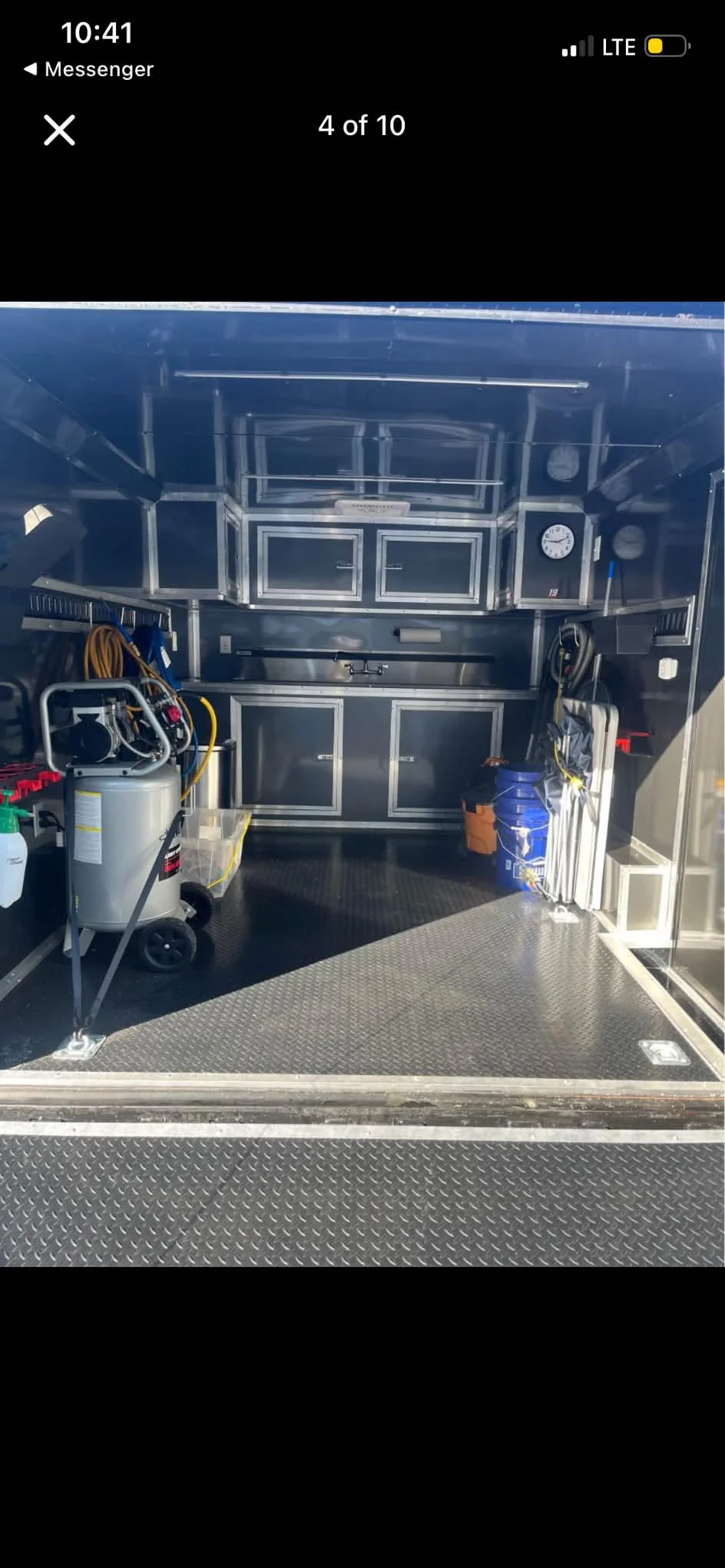 Interior of a metallic work trailer with storage cabinets, cleaning supplies, equipment, and tools.