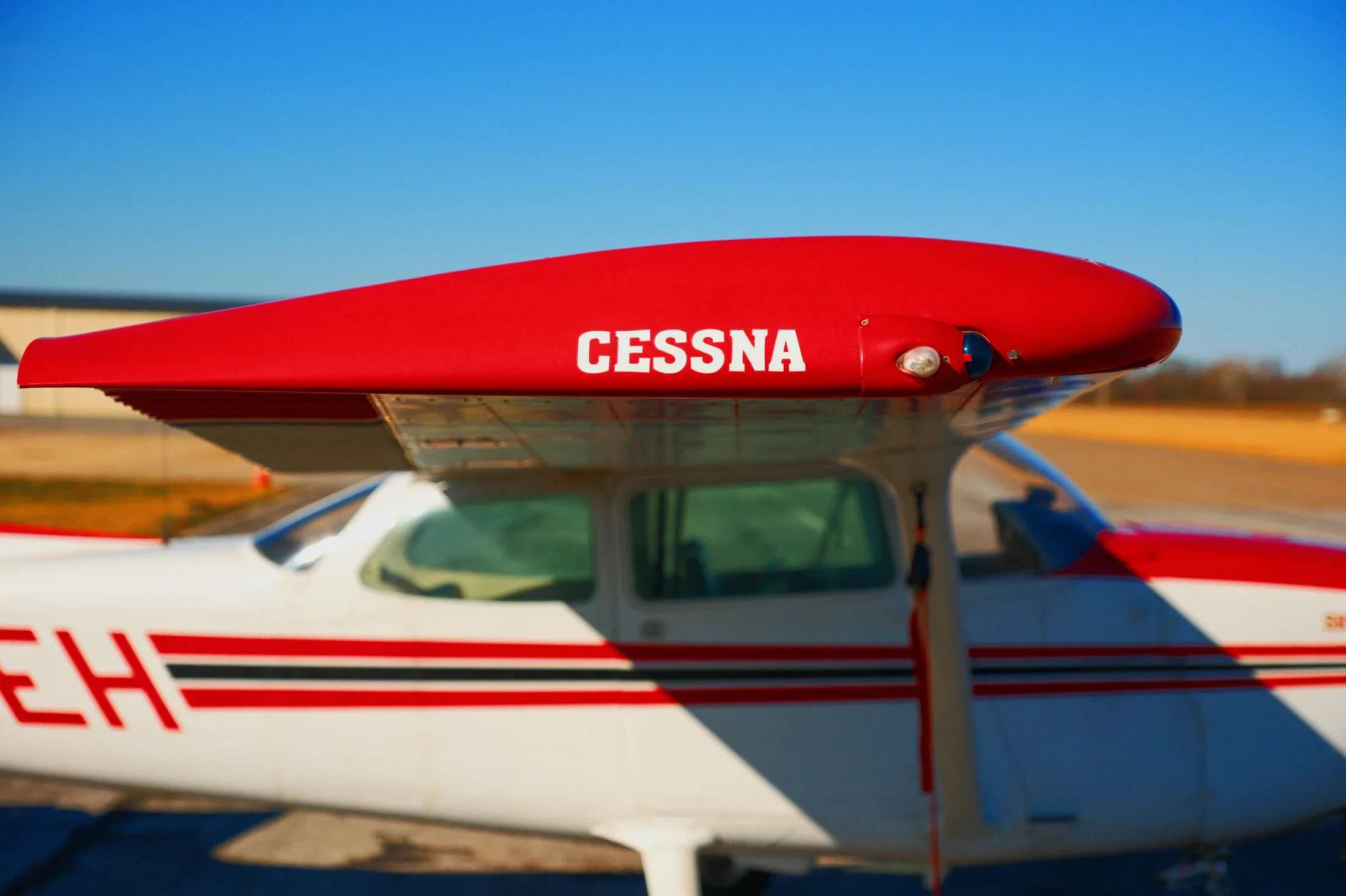 Close-up of a red Cessna airplane's wing and fuselage, with a clear blue sky in the background.