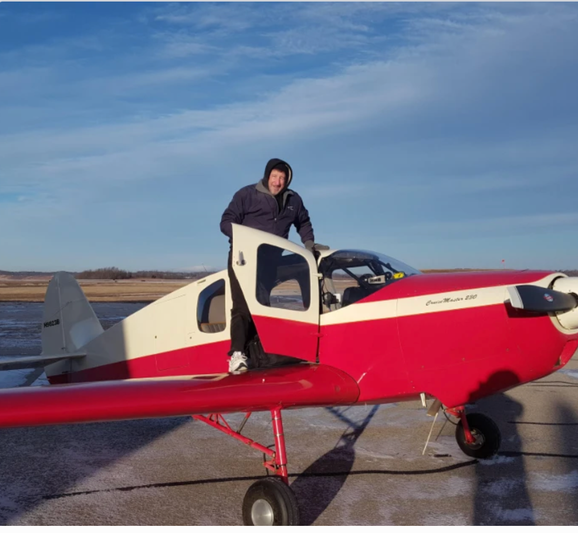 A person standing next to a small red and white airplane on a runway with a clear sky in the background.