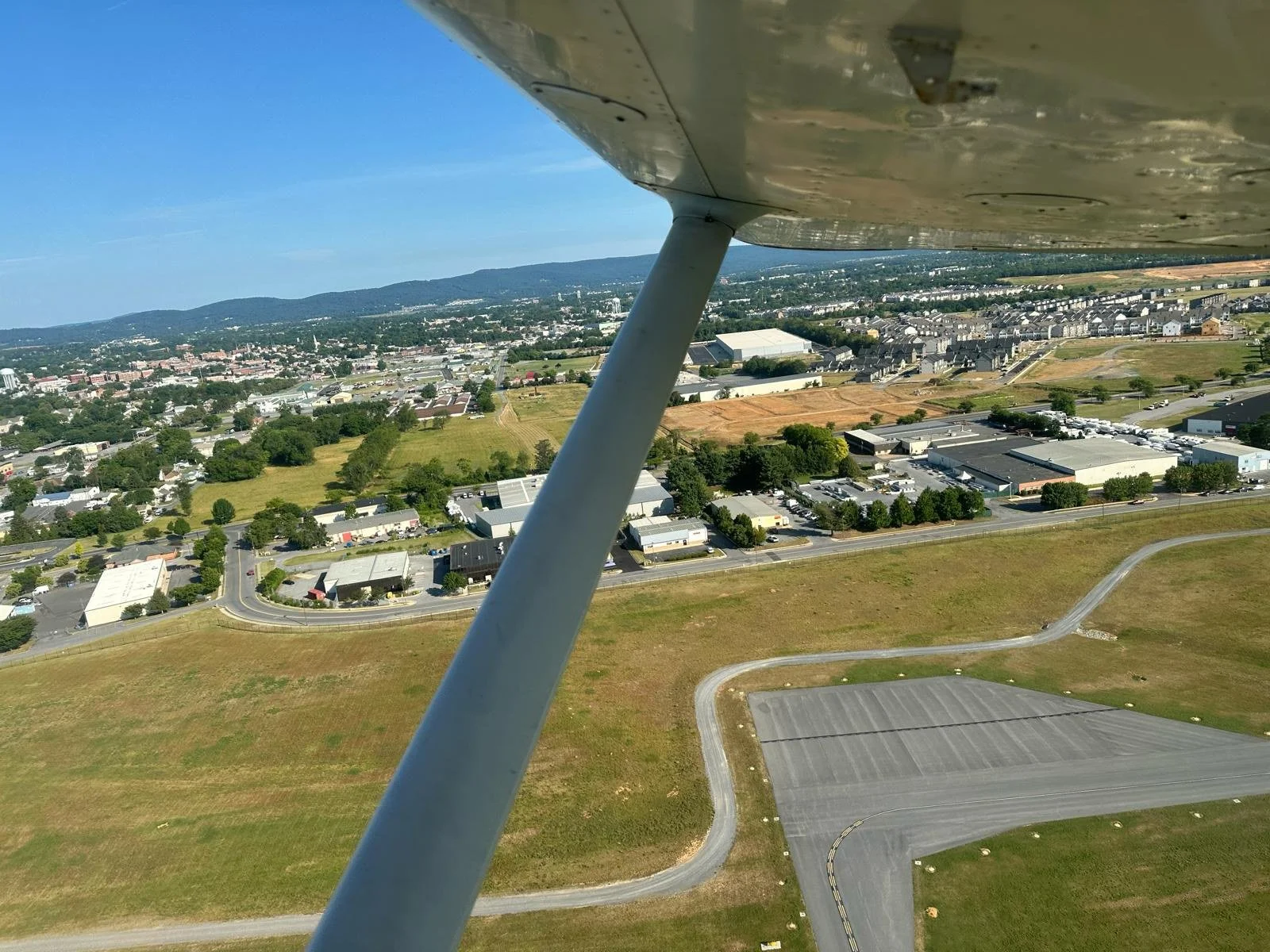 Aerial view of a town and surrounding landscape taken from an airplane, with part of the airplane wing in the foreground.