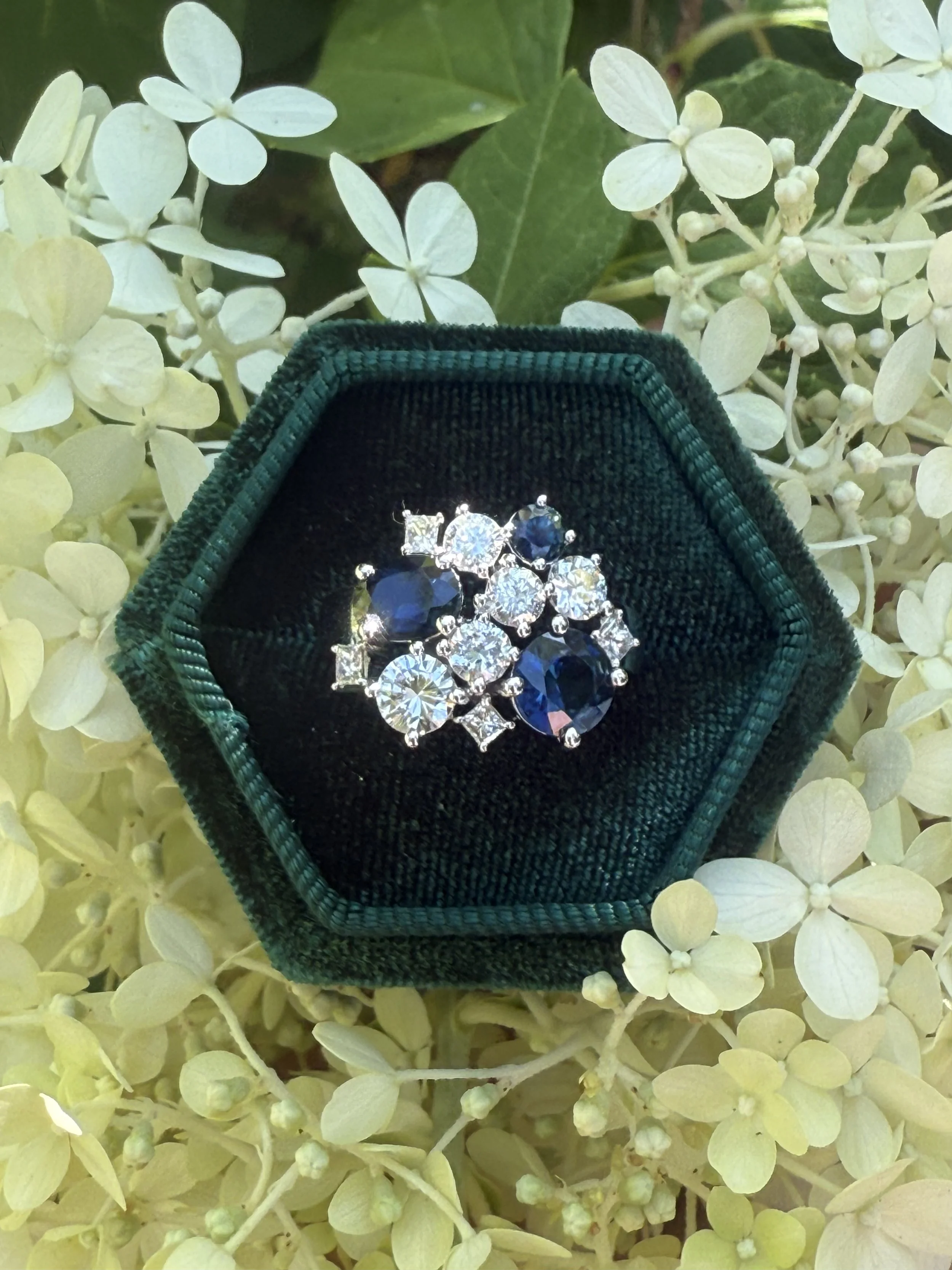 Custom 14K white gold cluster ring set with diamond and sapphire made with gemstones from several pieces of the client’s family jewelry spanning generations.