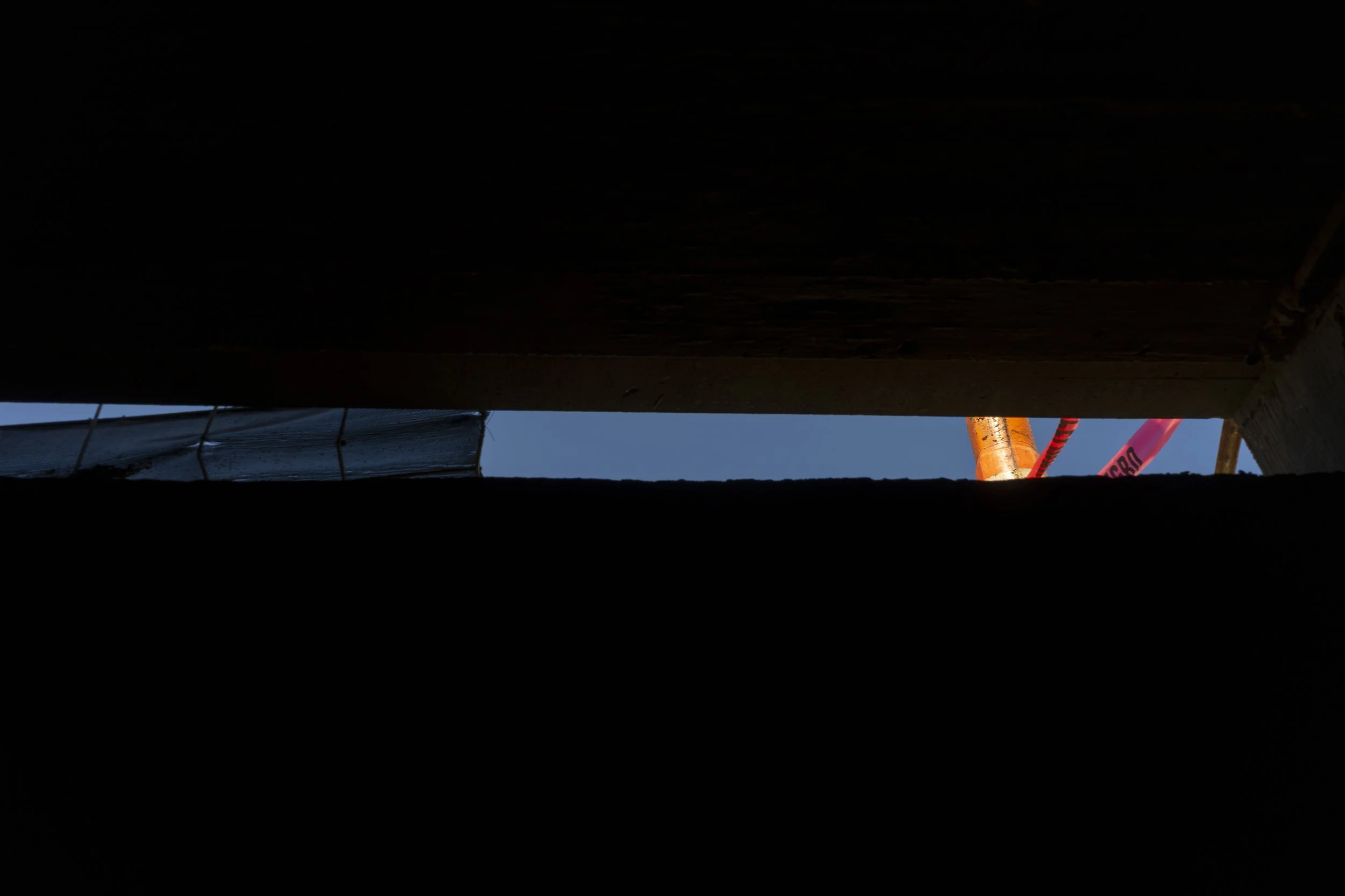 Dark construction area with orange safety pipe and warning tape, viewed from below.