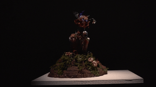 A detailed sculpture depicting a figure emerging from rocks and moss against a black background.