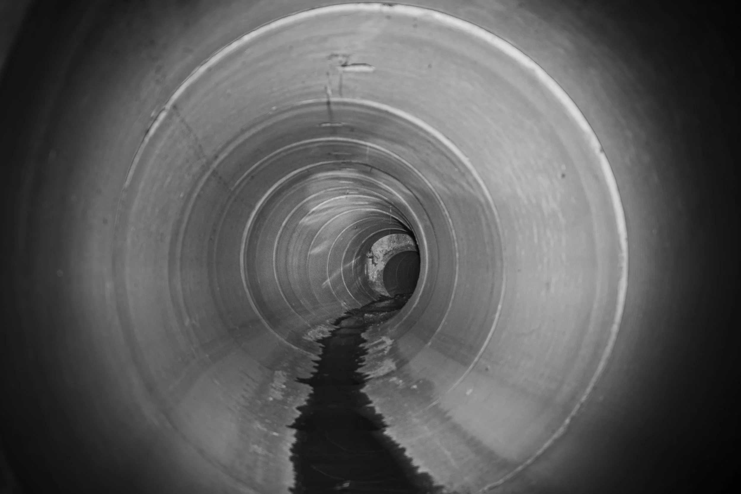 View inside a large, empty metal pipe with water at the bottom, extending into the distance.