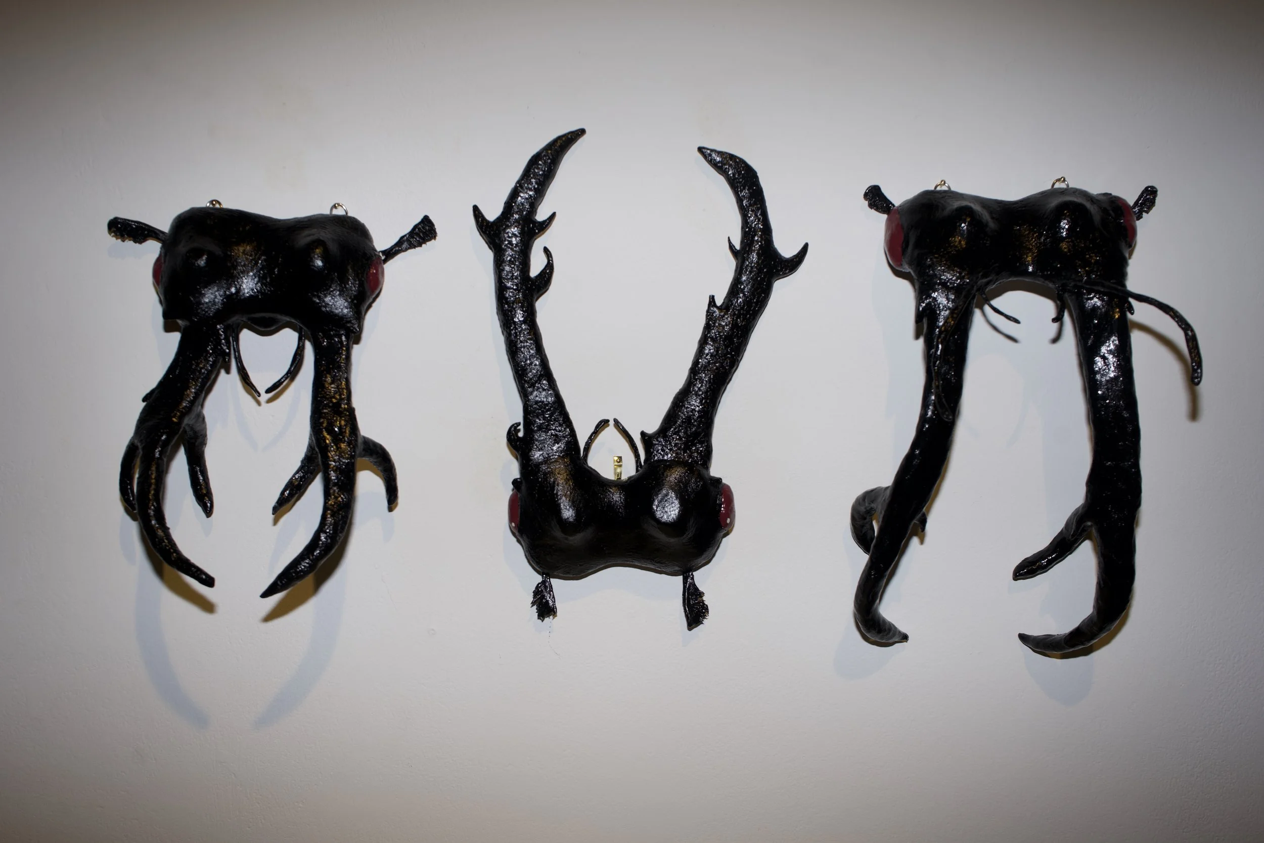 Artistic sculpture of a deer's head with elongated antlers, made of dark, glossy material, mounted on a white wall.