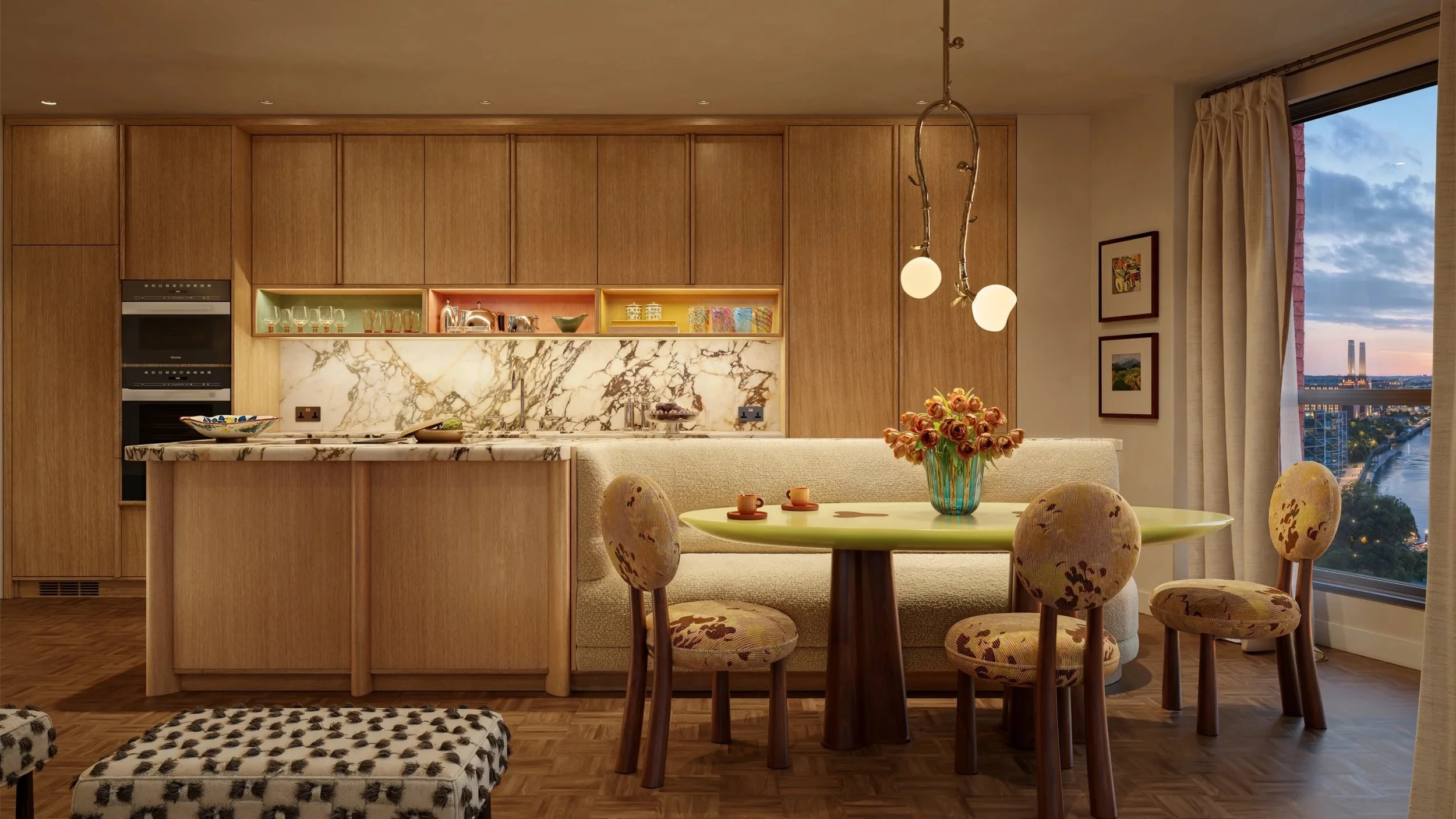 Interior view of a modern kitchen and dining area with wooden cabinets, marble backsplash, round dining table with flowers, and chairs, with a large window showing a cityscape at sunset.