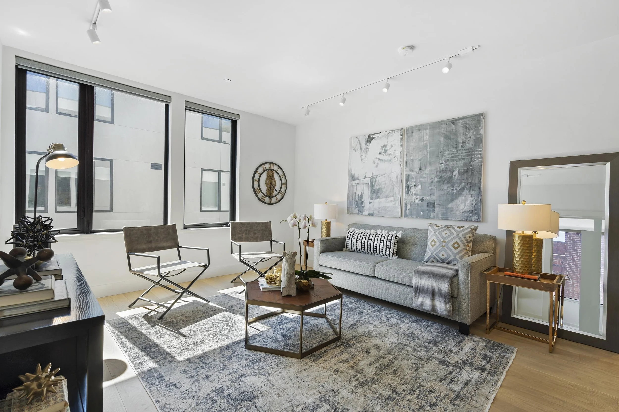 Modern living room with large windows, abstract artwork, gray sofa, and multiple decorative items.