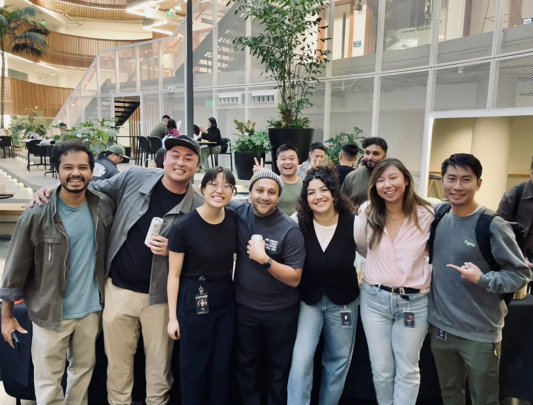 A group of people smiling and posing for a photo at an indoor event space with plants and a staircase in the background.