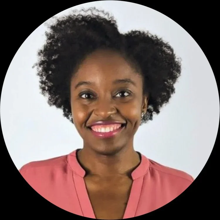 Smiling woman with natural curly hair wearing a pink blouse against a white background.