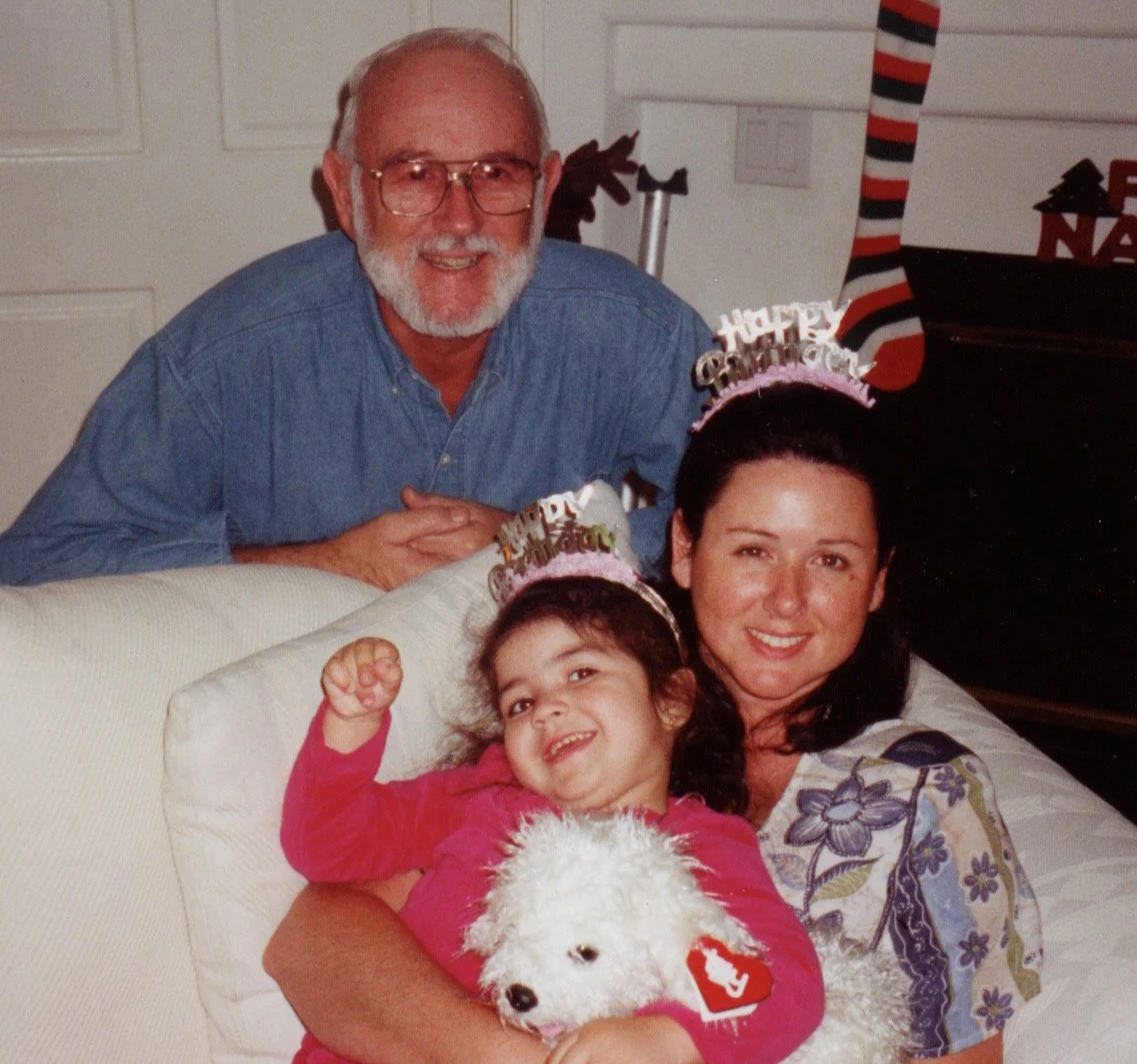 A family celebrating Christmas, including an older man and a woman with a young girl and a dog, wearing birthday hats that say 'Happy Birthday' in a cozy room.