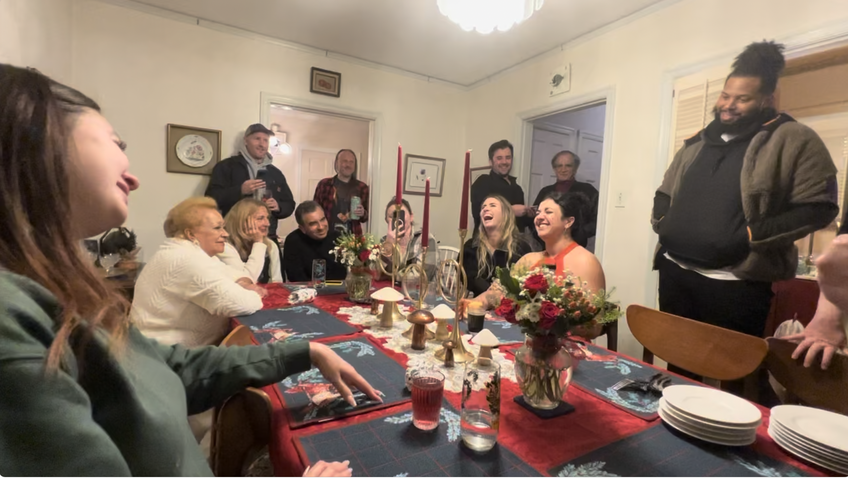 A group of people gathered around a festive dinner table, laughing and smiling during a celebration in a cozy dining room.