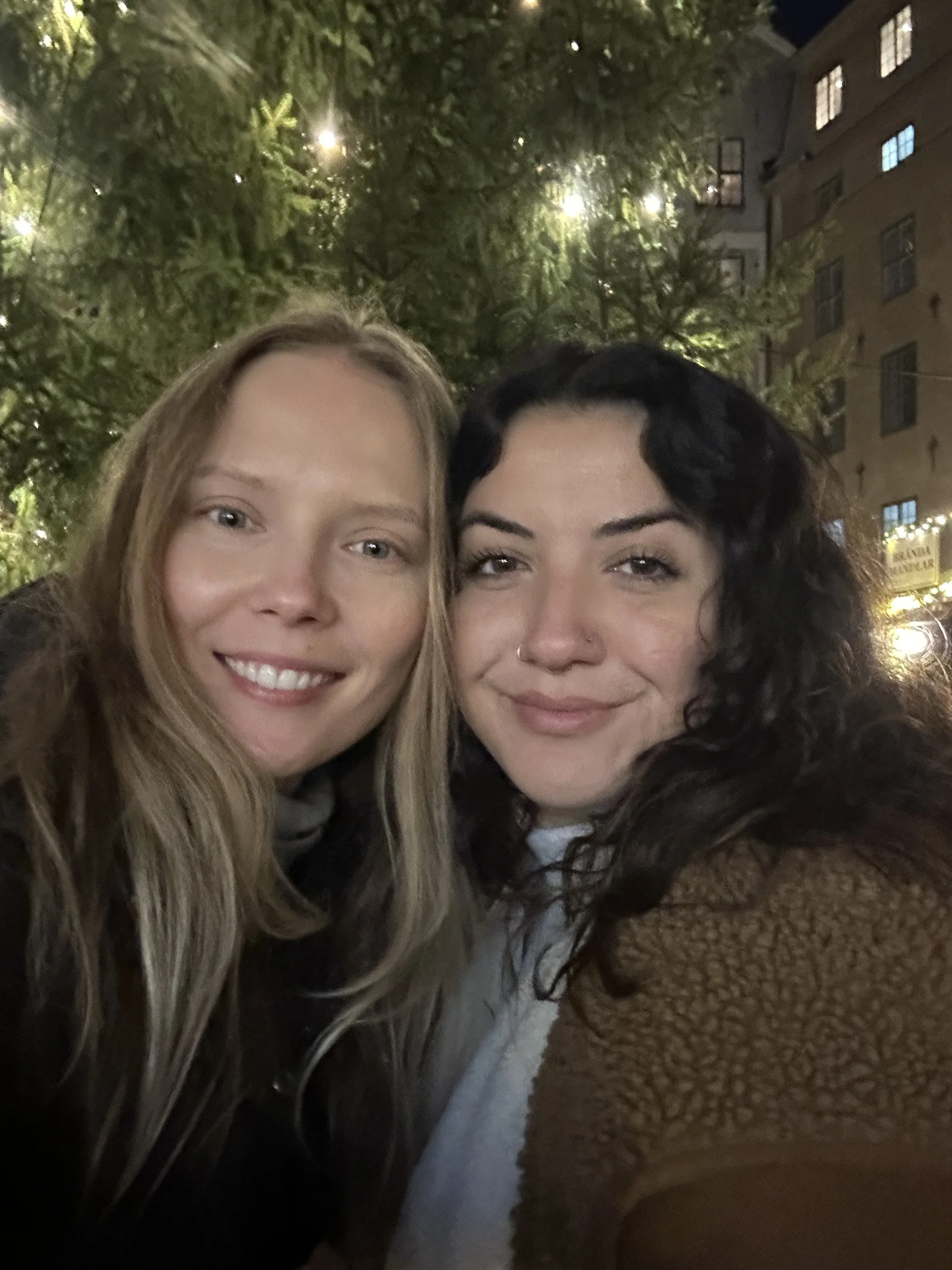 Two women smiling outdoors at night, with trees and building lights in the background.