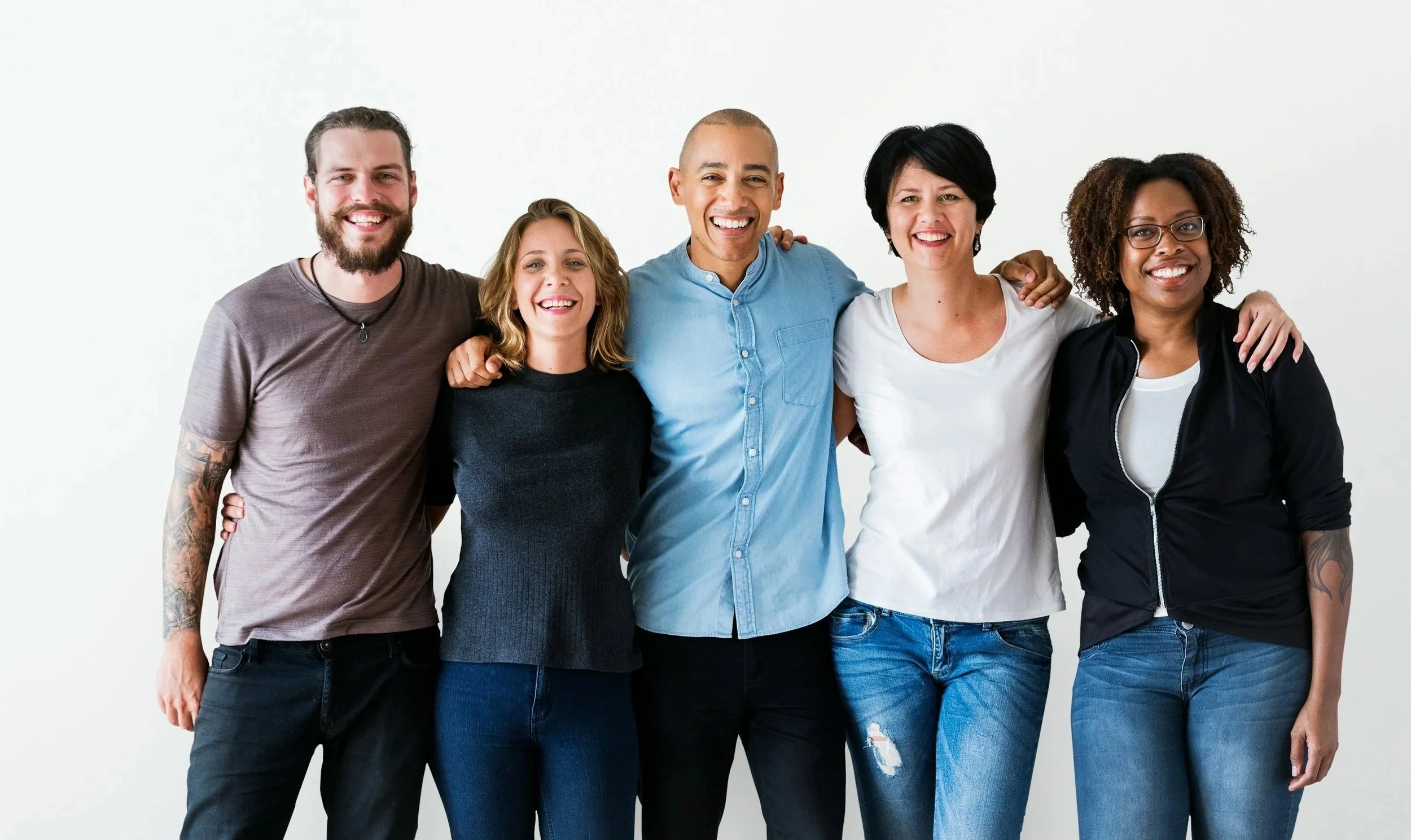 Six diverse young adults standing close together, smiling, and posing with arms around each other against a plain white background.