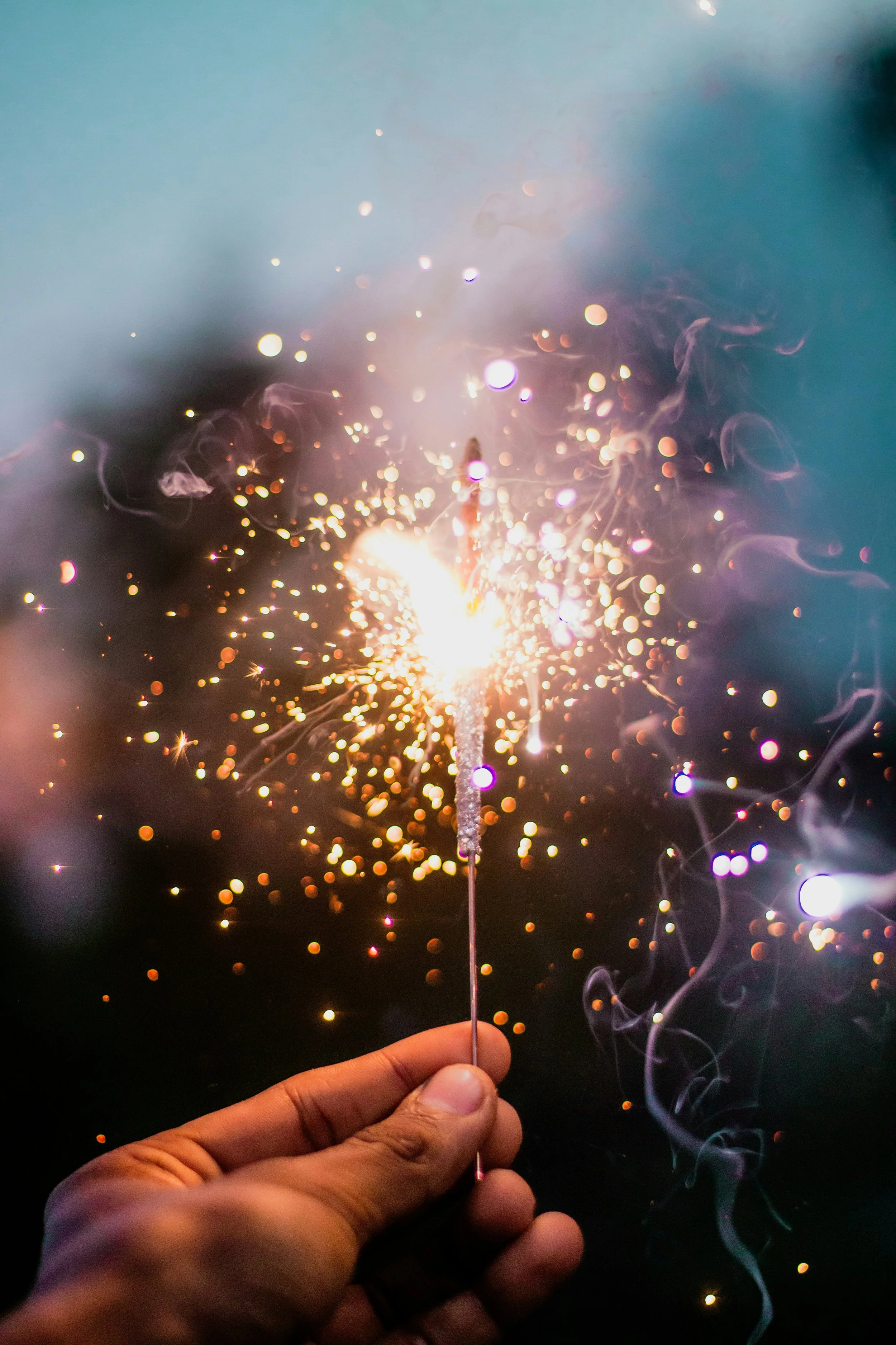 Person holding a sparkler at night with sparks and light trails.