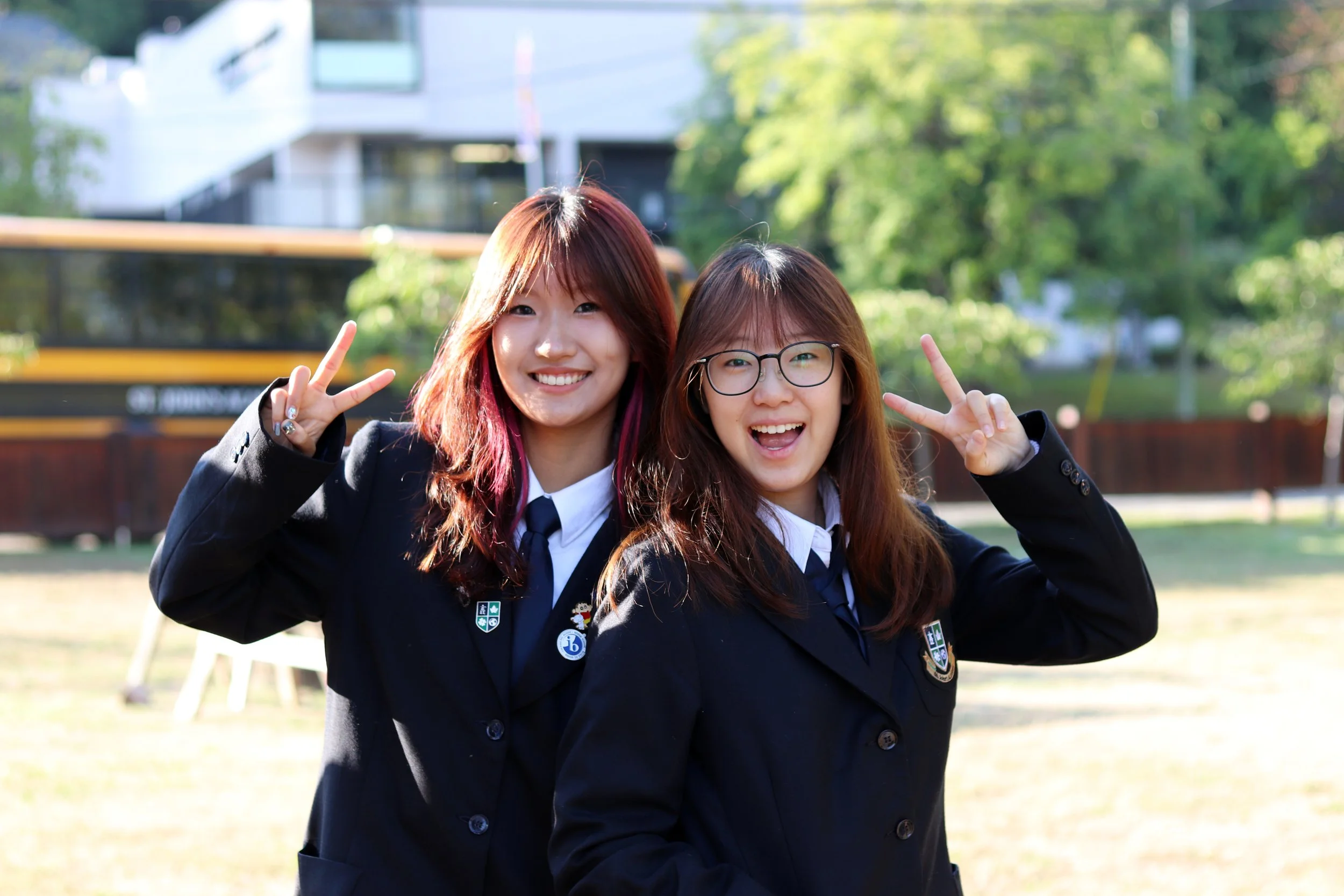 Two smiling schoolgirls in uniforms posing outdoors and making peace signs