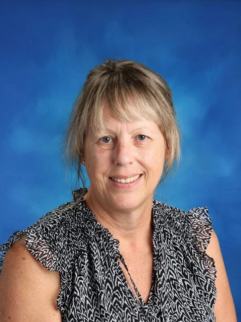 Portrait of a smiling middle woman with short blonde hair wearing a black-and-white patterned blouse against a blue background