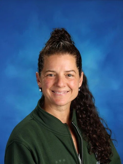 Professional headshot of a smiling woman with curly brown hair against a blue studio background