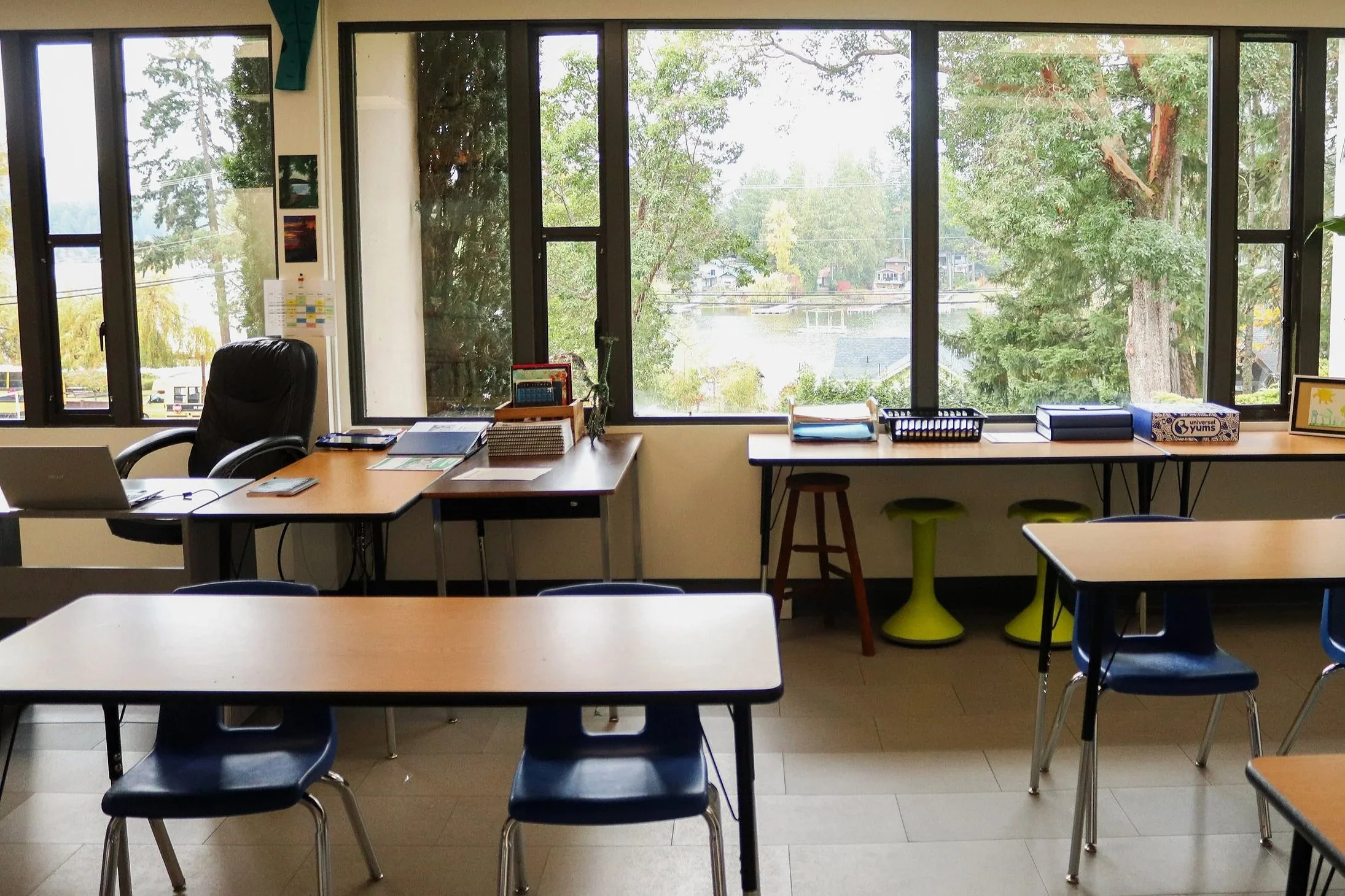 Bright classroom with desks, chairs, teacher’s workstation, and large windows overlooking a tree-lined lake